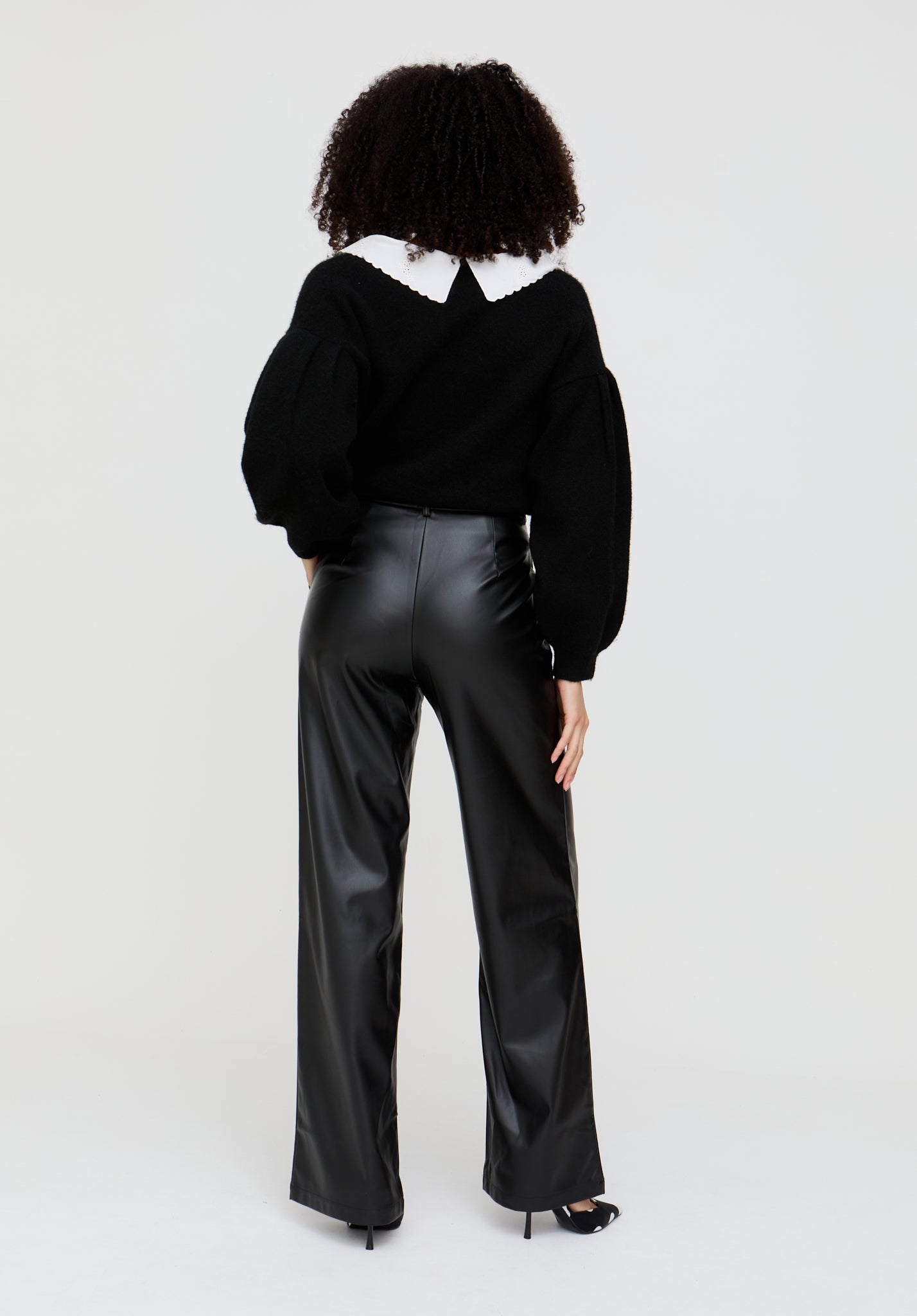 Person wearing a black outfit with a white collar on a light gray background