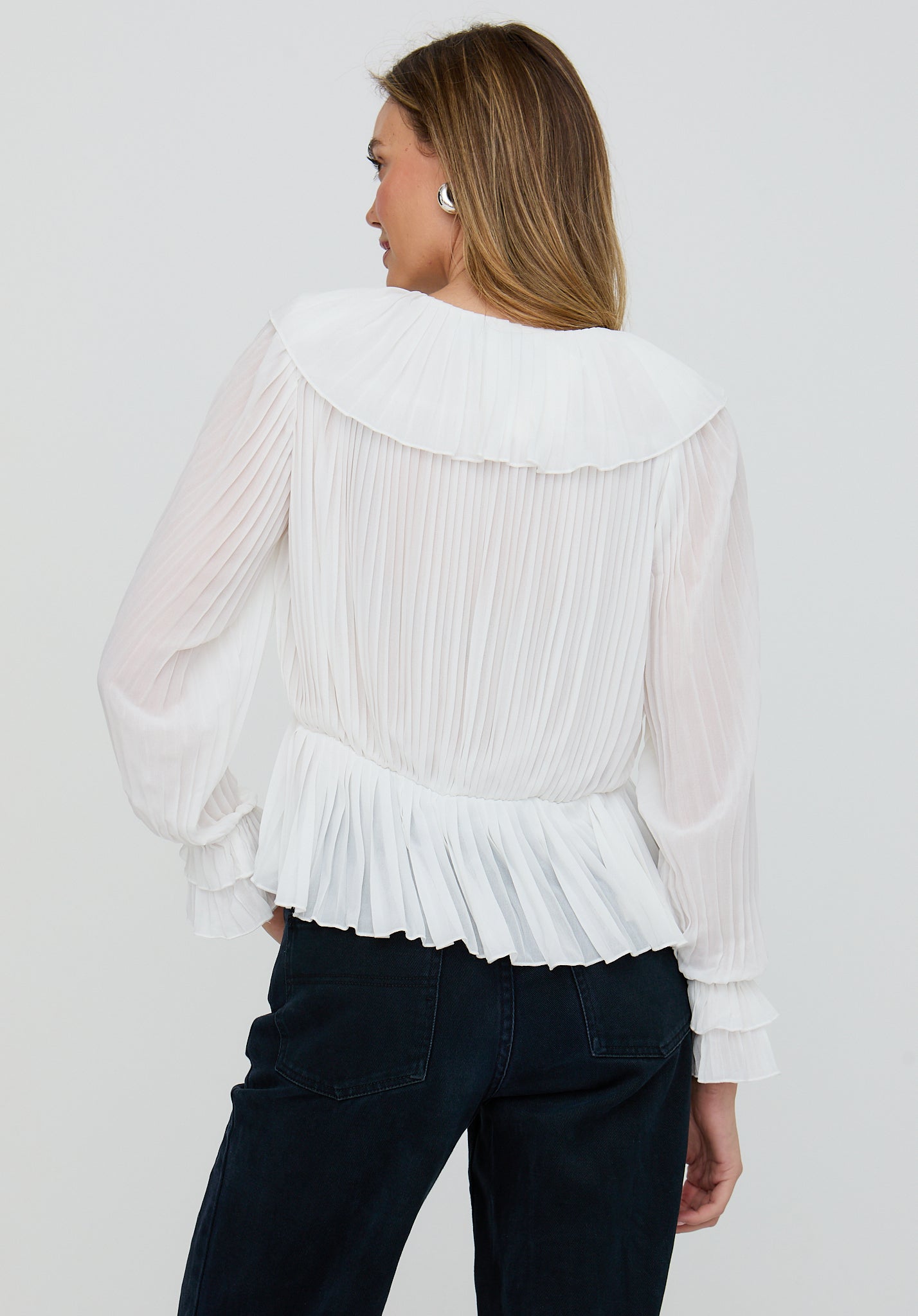 Woman wearing a white pleated blouse with a plain background