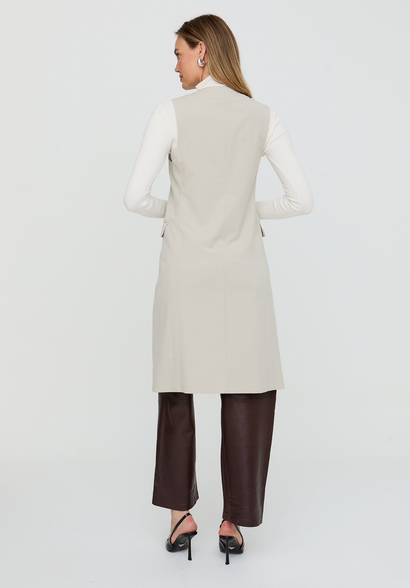 Woman wearing a long beige coat and brown pants on a white background