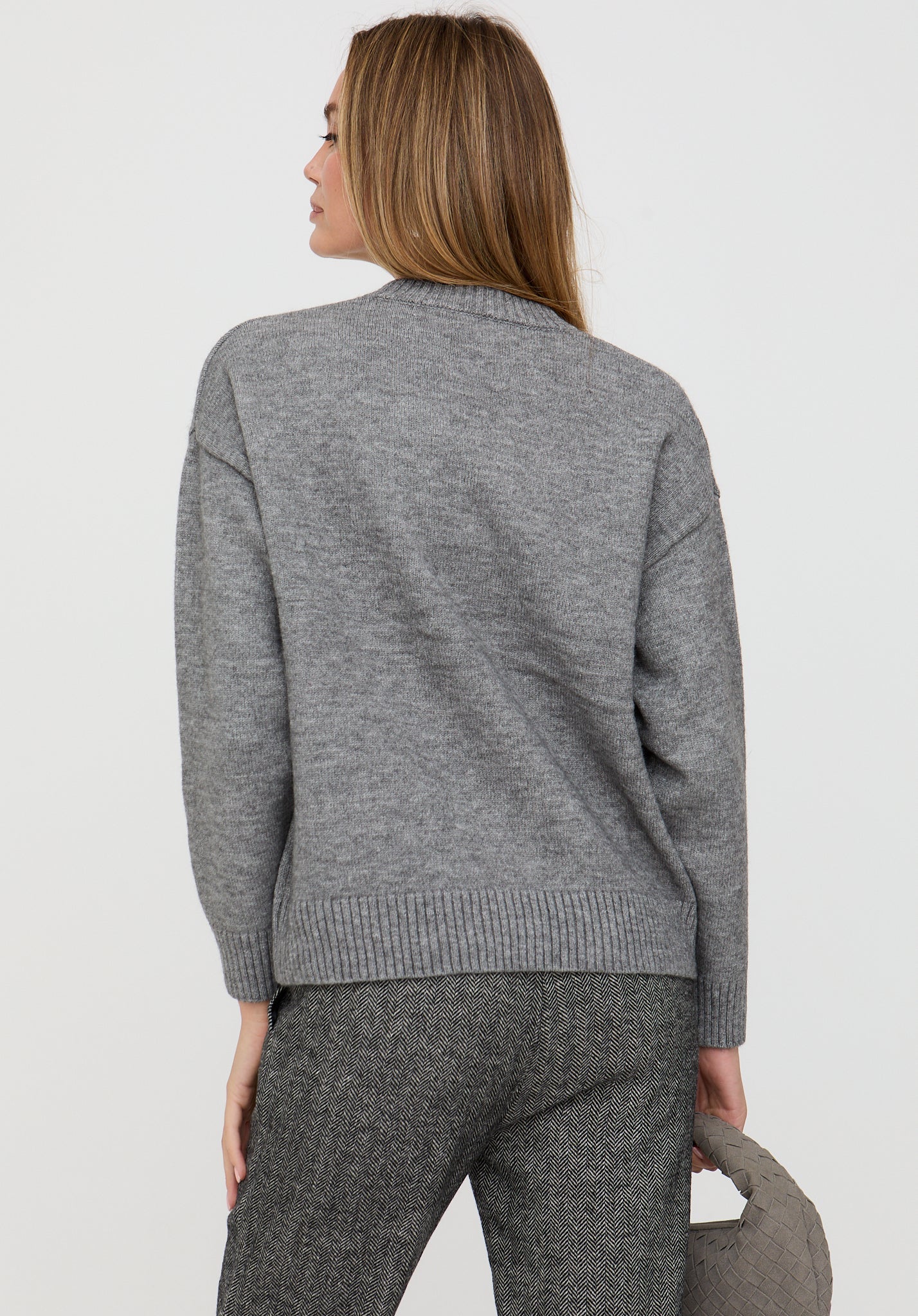 Woman wearing a gray sweater and pants against a white background
