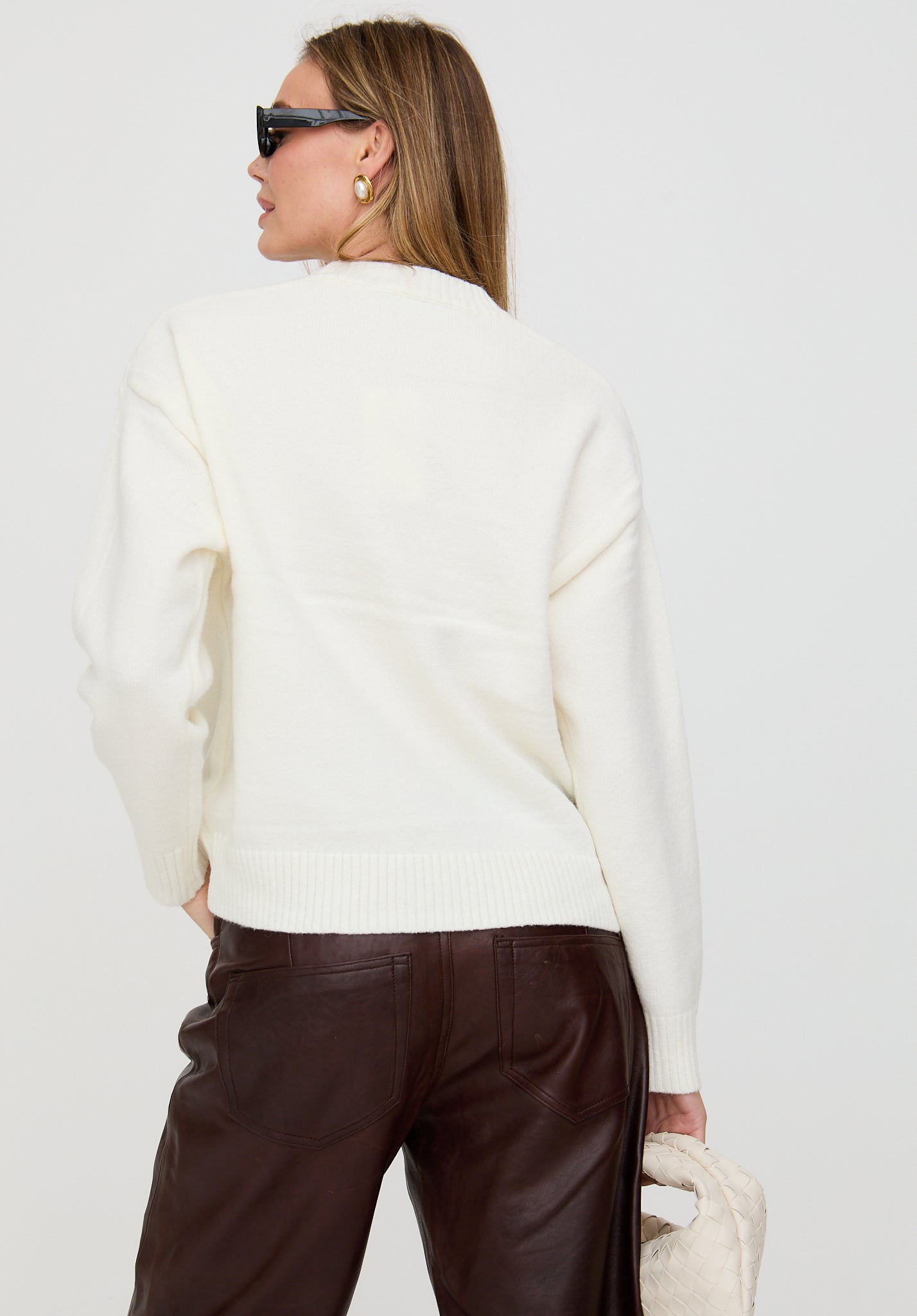 Woman wearing a white sweater and brown pants against a plain background
