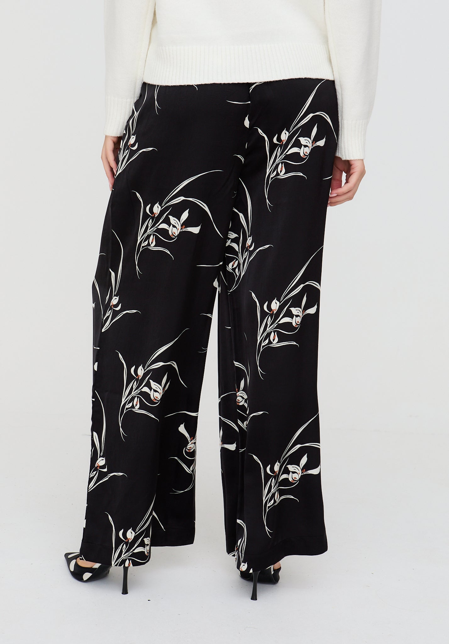 Black floral-patterned pants worn by a person on a white background