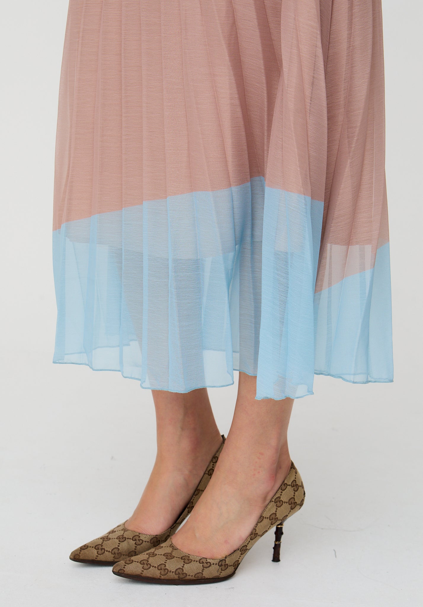 Person wearing a two-tone skirt with pink top and blue bottom, paired with patterned high heels on a white background.