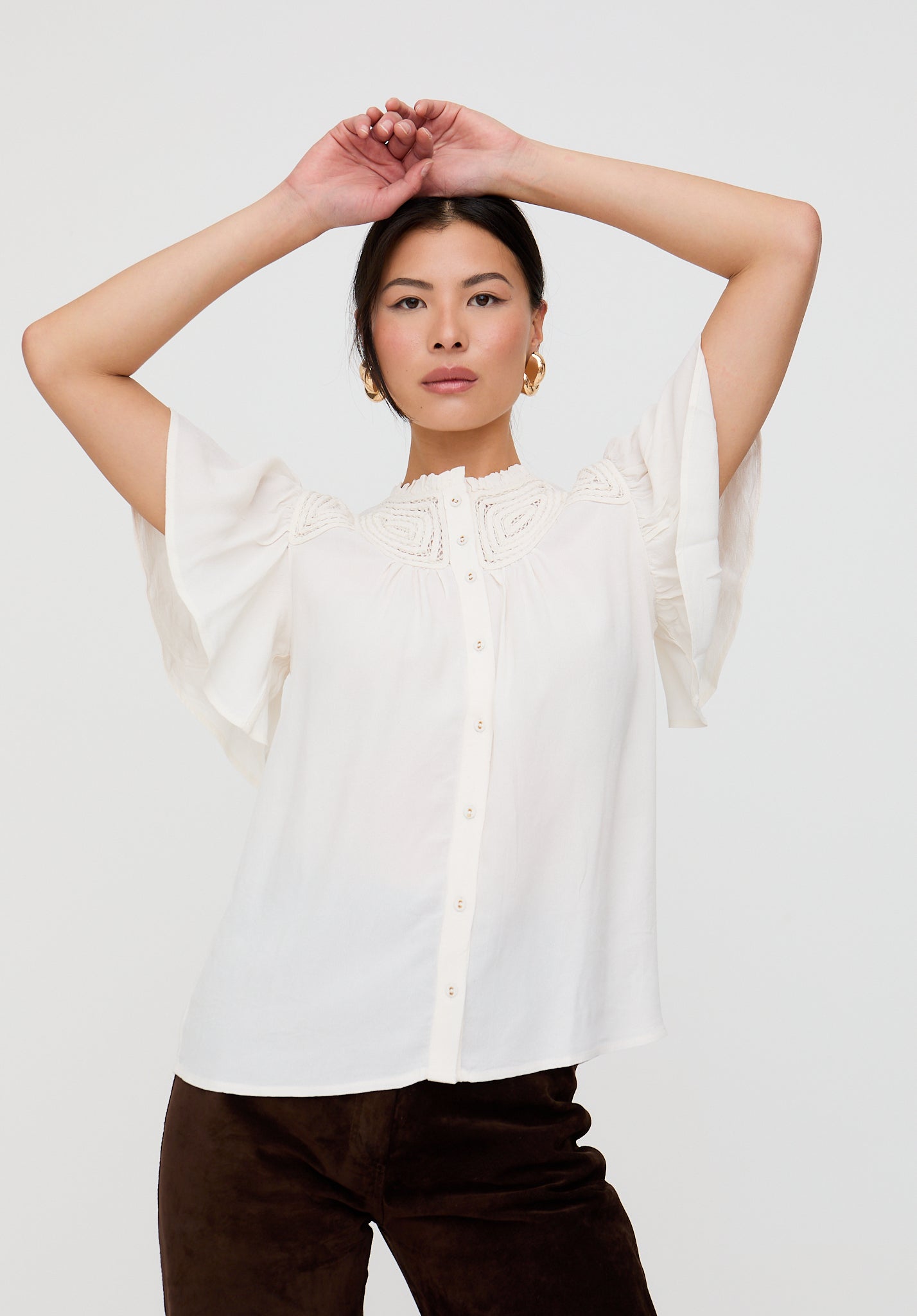 Woman wearing a white blouse with sheer sleeves against a plain background