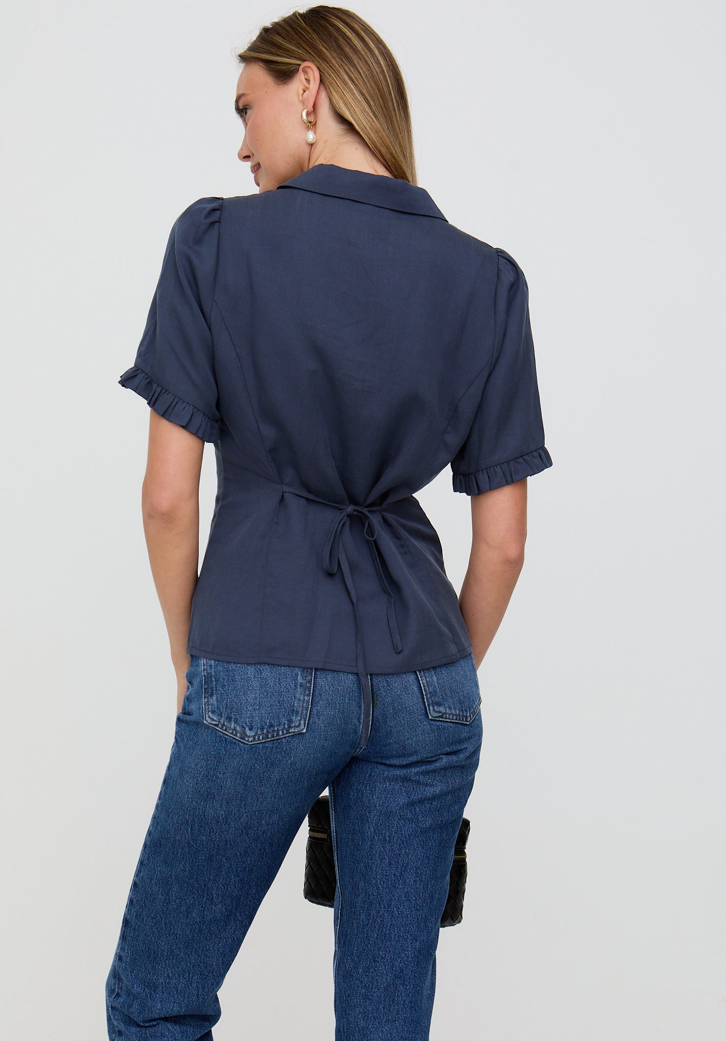 Woman wearing a navy blue shirt and jeans on a light gray background