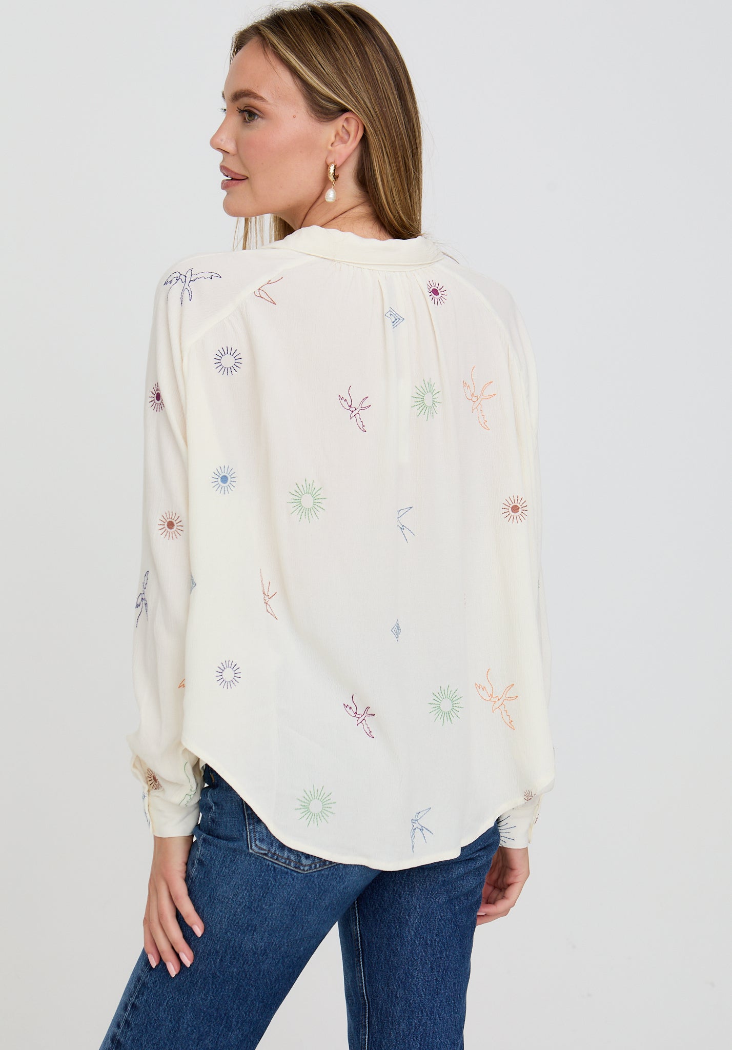 Woman wearing a white blouse with colorful floral embroidery on a plain background