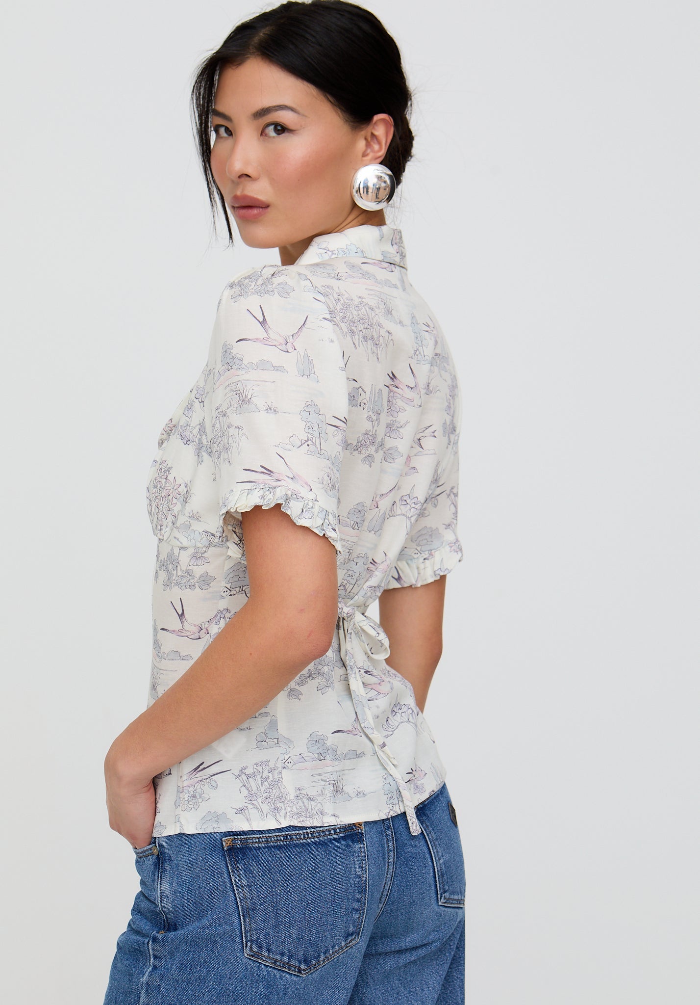 Woman wearing a floral blouse and blue jeans against a white background