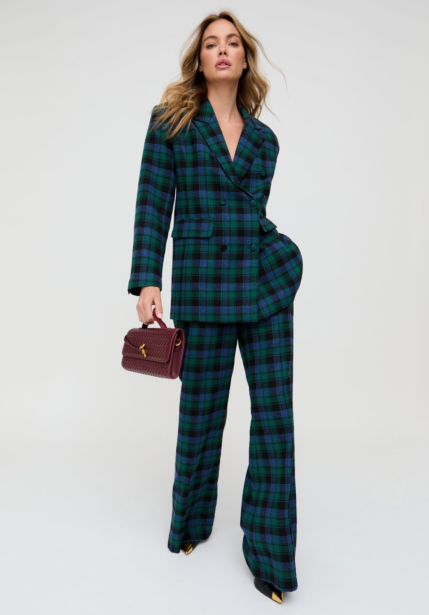 Woman wearing a green plaid suit holding a red handbag on a white background