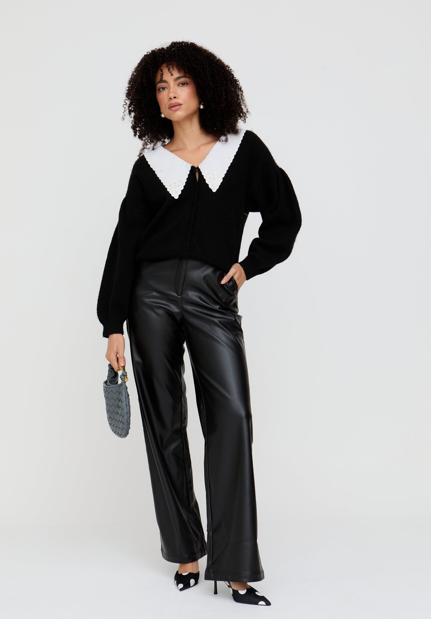 Woman wearing a black sweater with a white collar and black leather pants on a white background