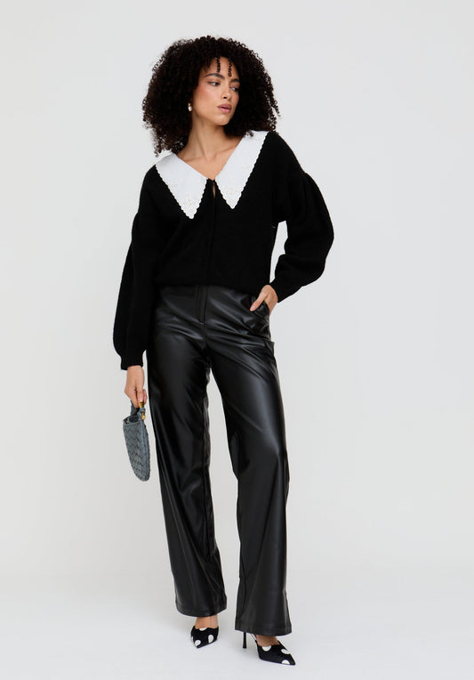 Woman wearing a black sweater with a white collar and black pants on a white background