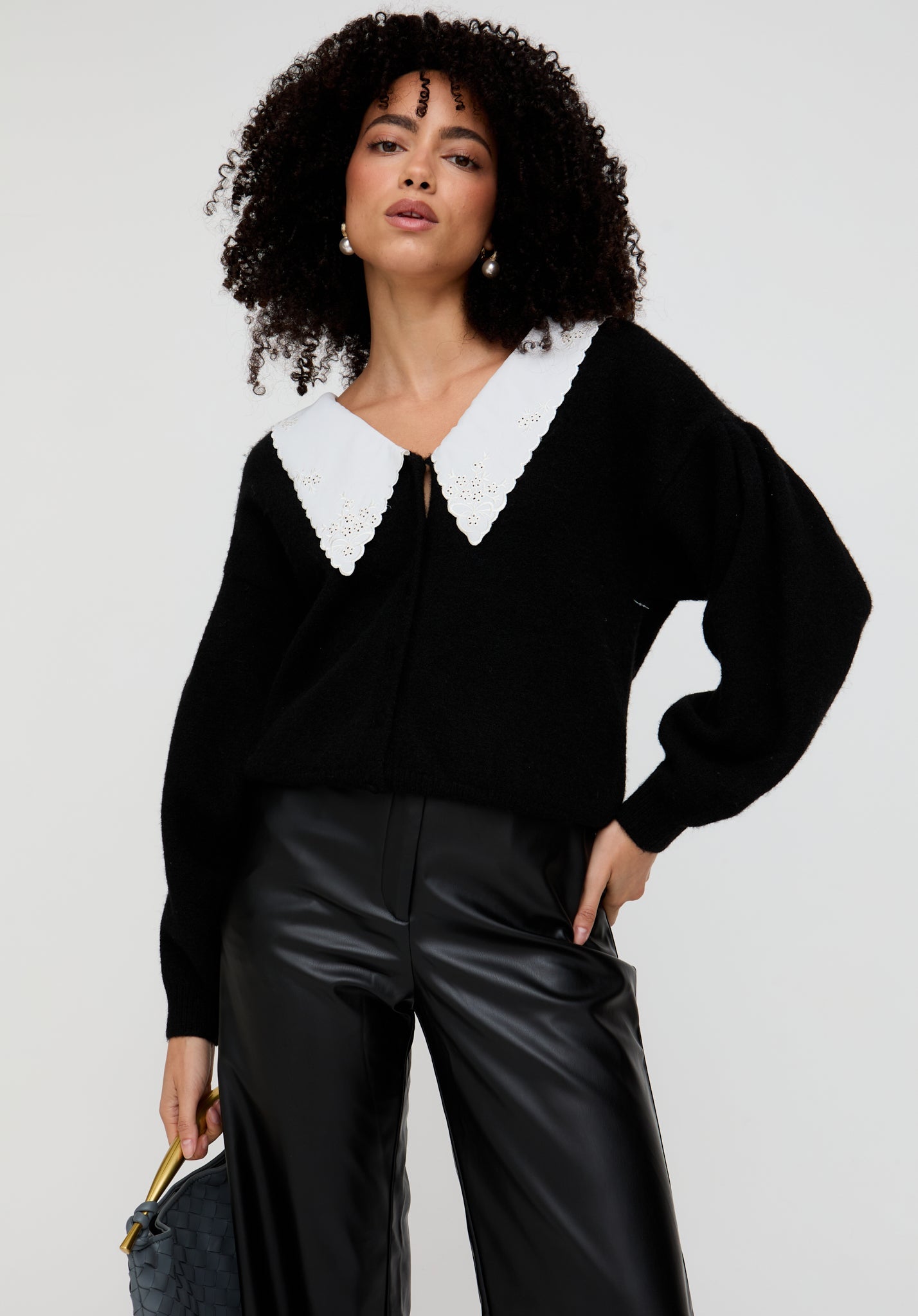 Woman wearing a black sweater with a white collar against a plain background