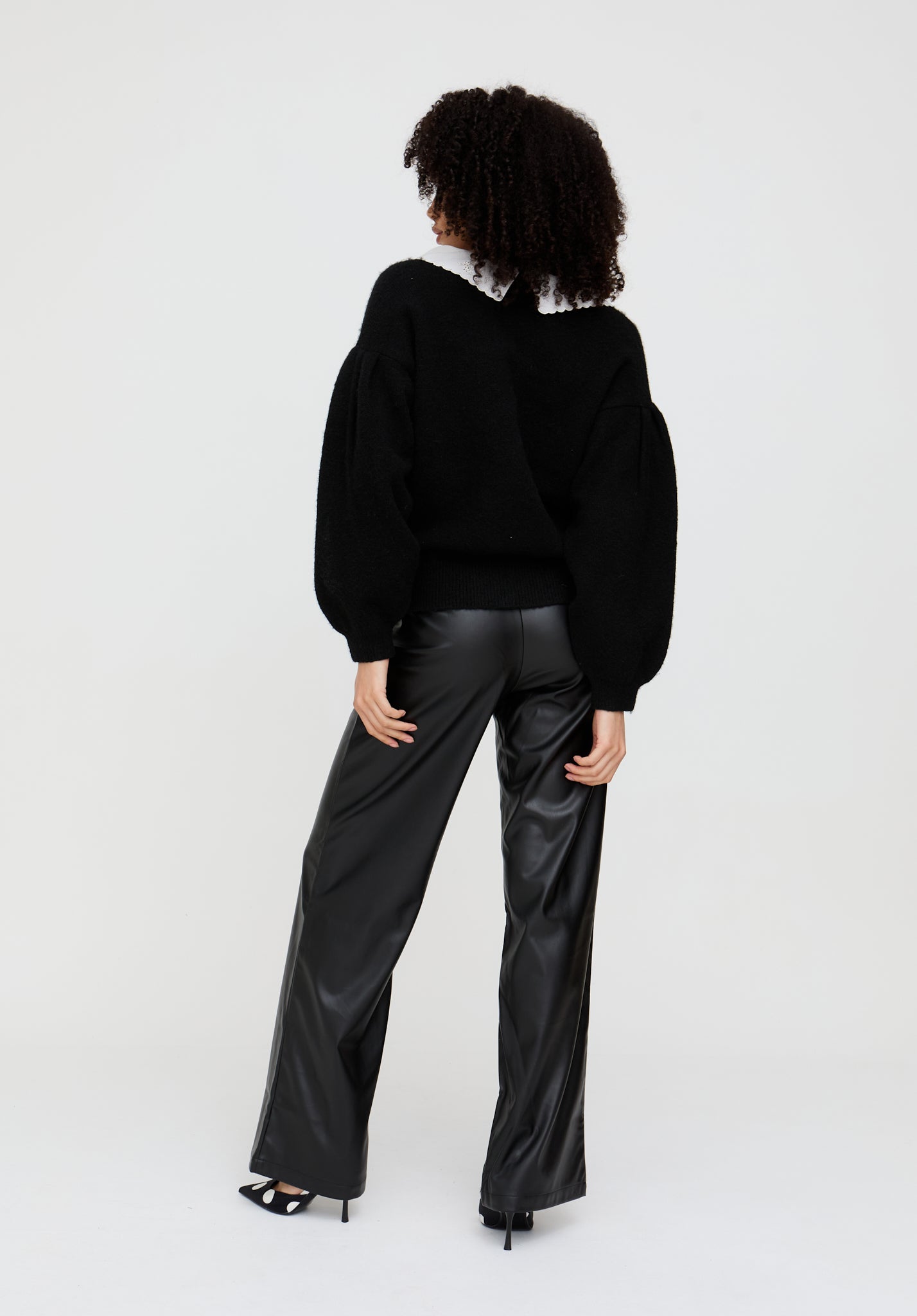 Person wearing a black sweater and black leather pants on a white background
