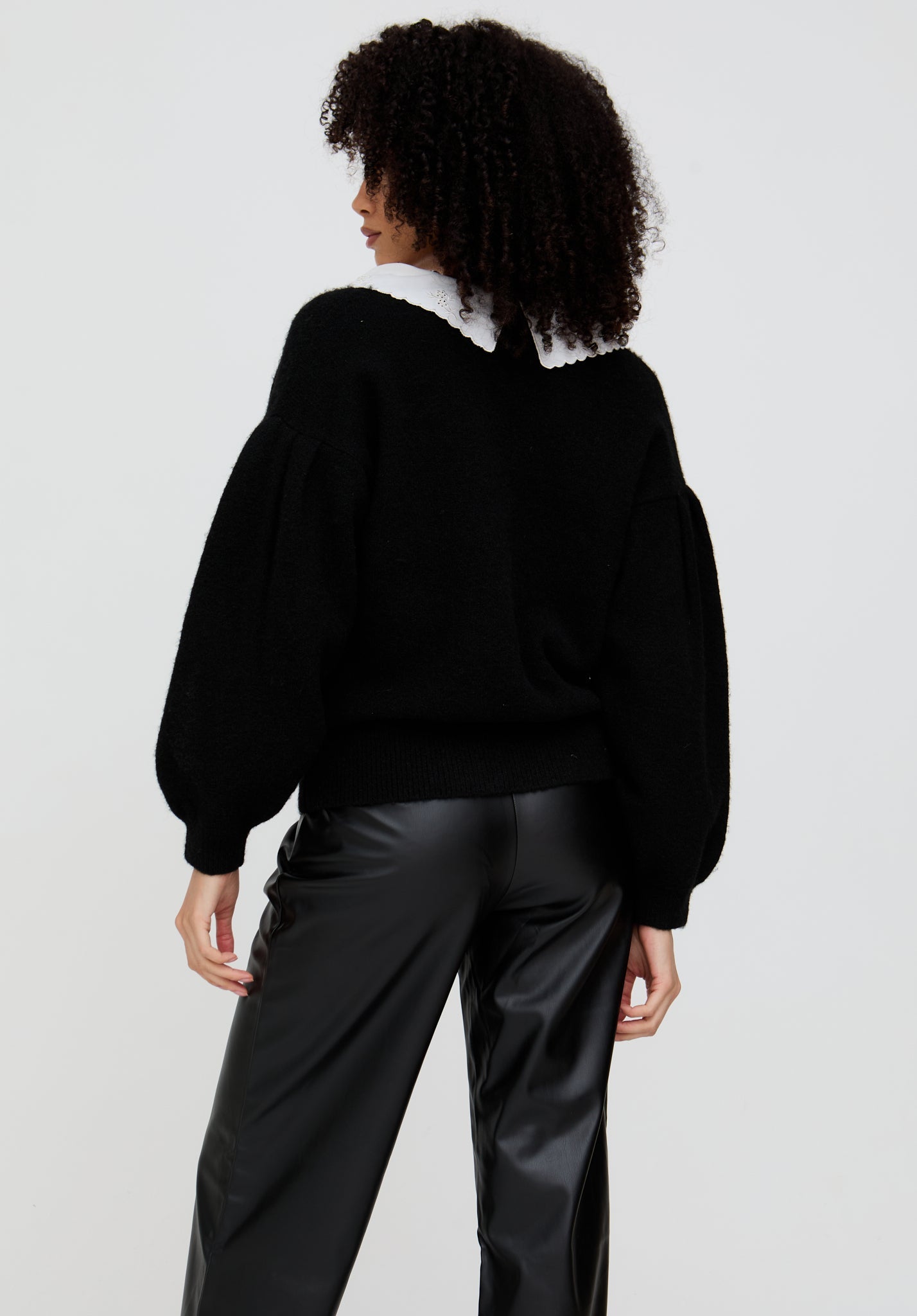 Person wearing a black sweater and black pants on a white background