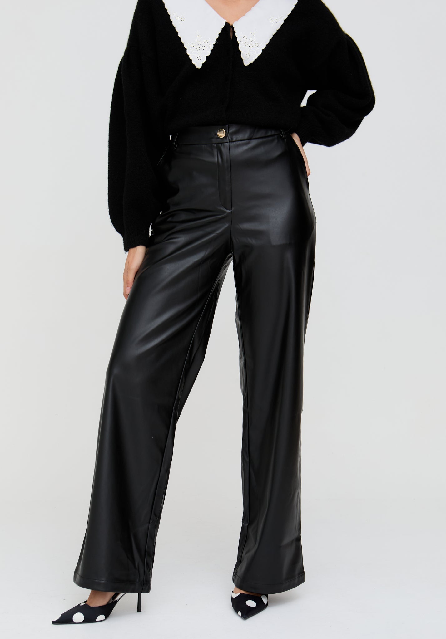 Person wearing a black outfit with a white collar and black leather pants on a light gray background