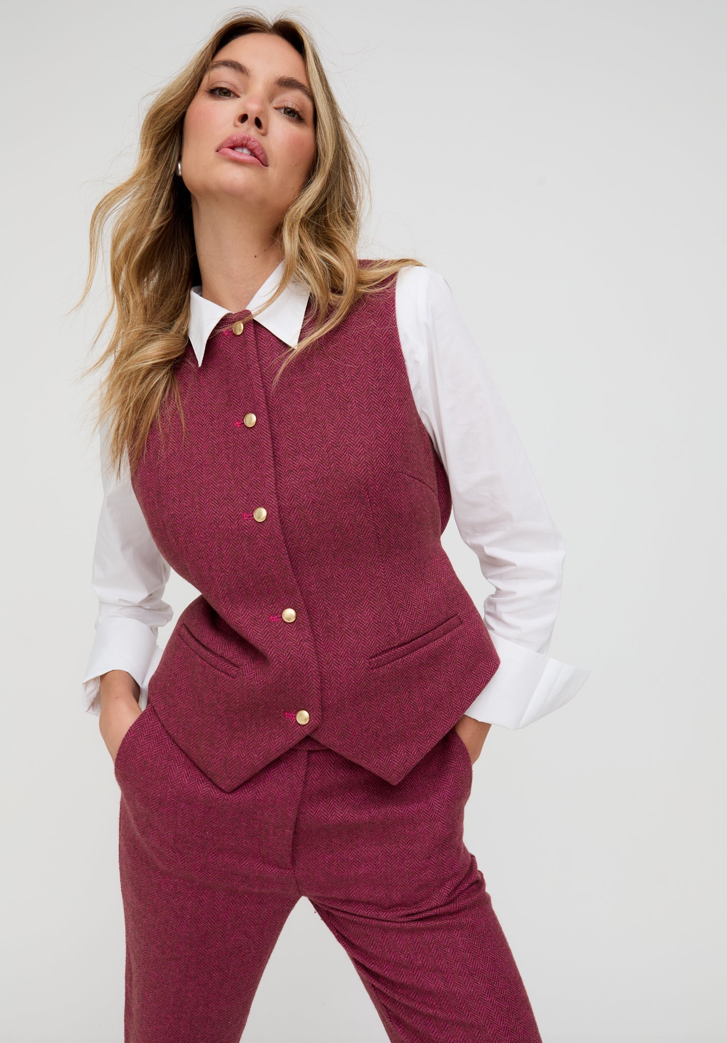 Woman wearing a burgundy suit with a white shirt on a plain background