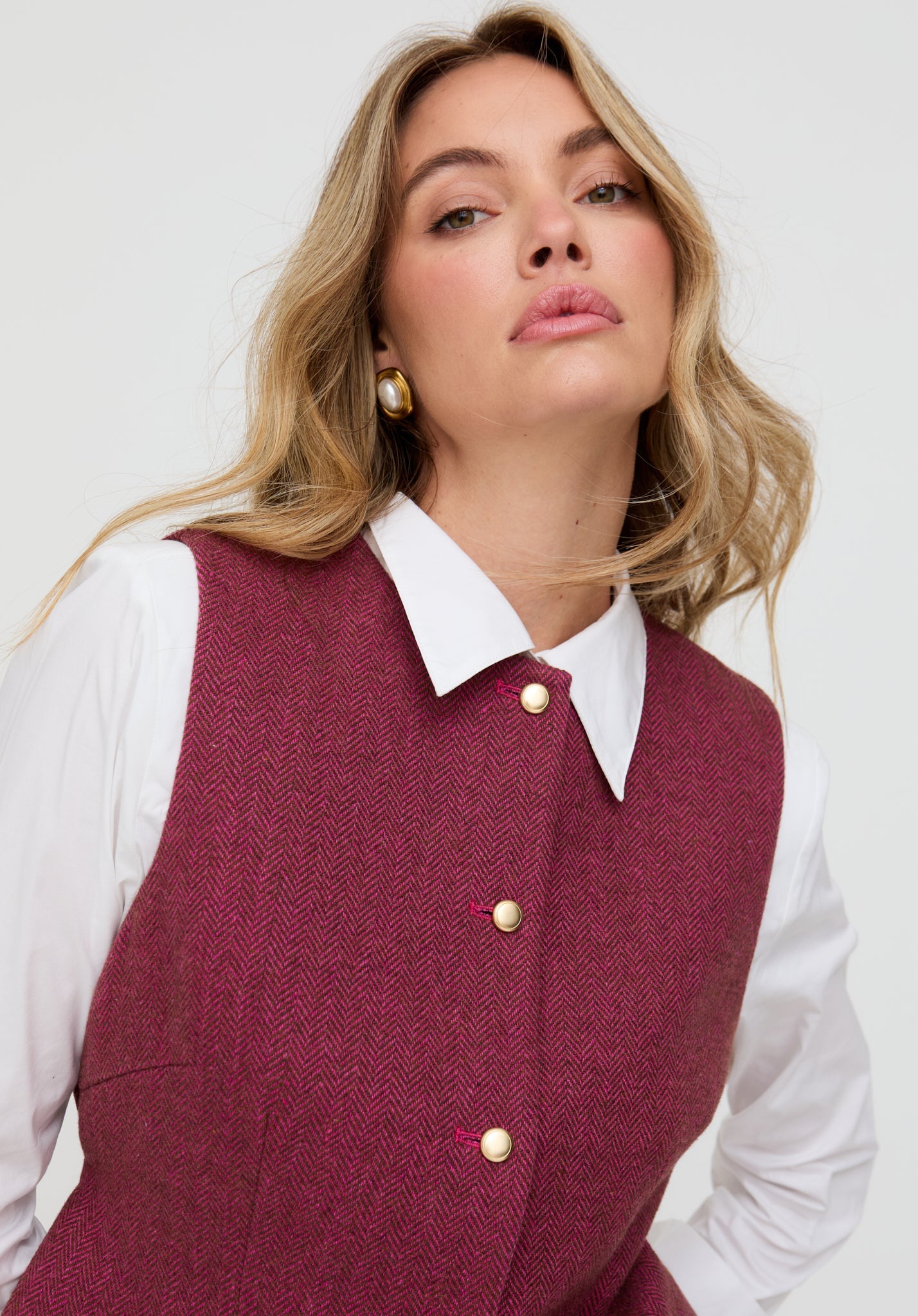 Woman wearing a maroon vest over a white shirt with a plain background