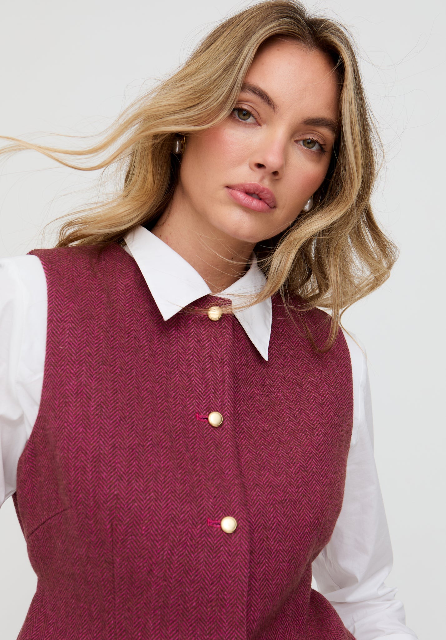 Woman wearing a burgundy vest over a white shirt on a plain background