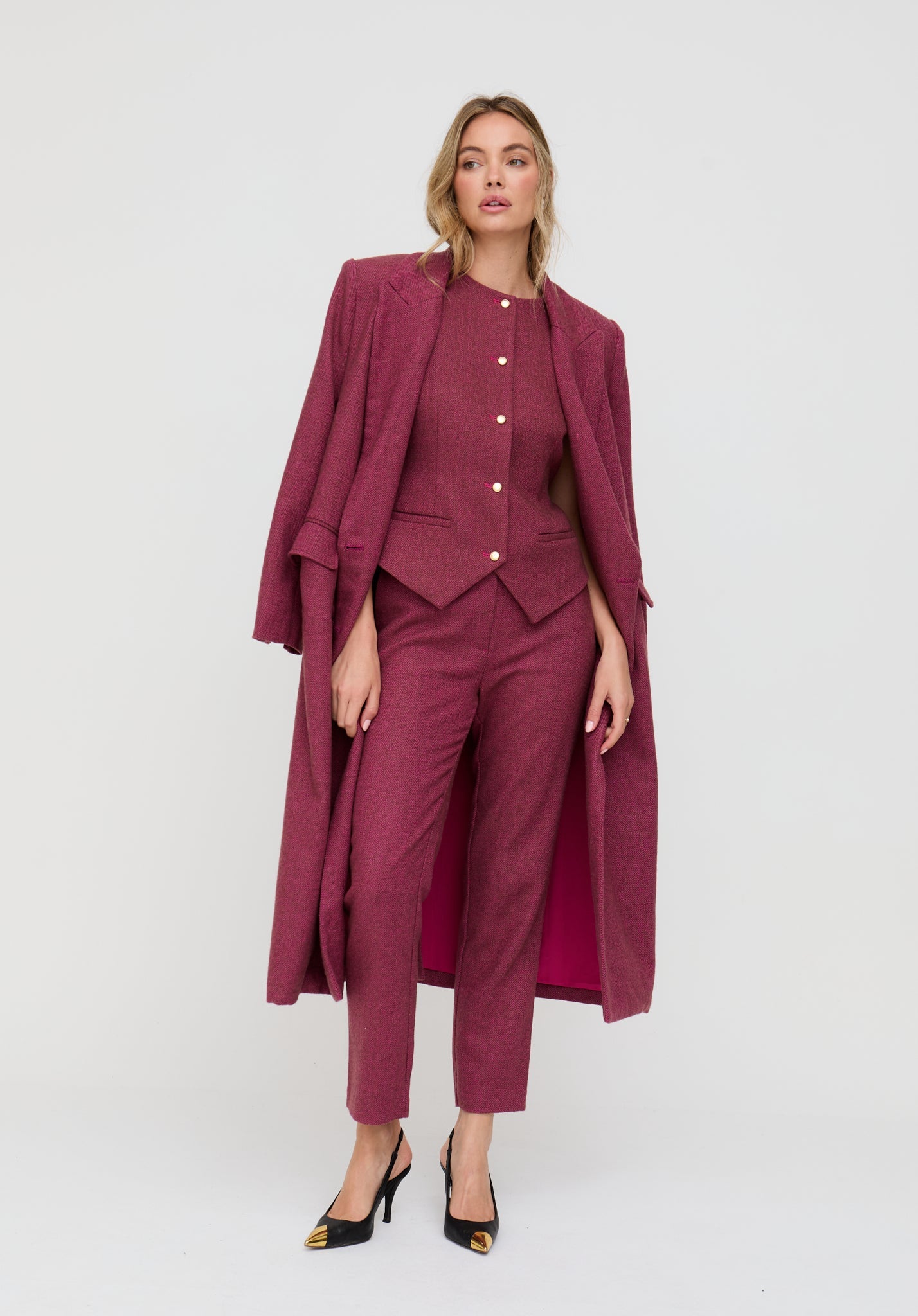 Woman wearing a burgundy suit with a long coat on a white background