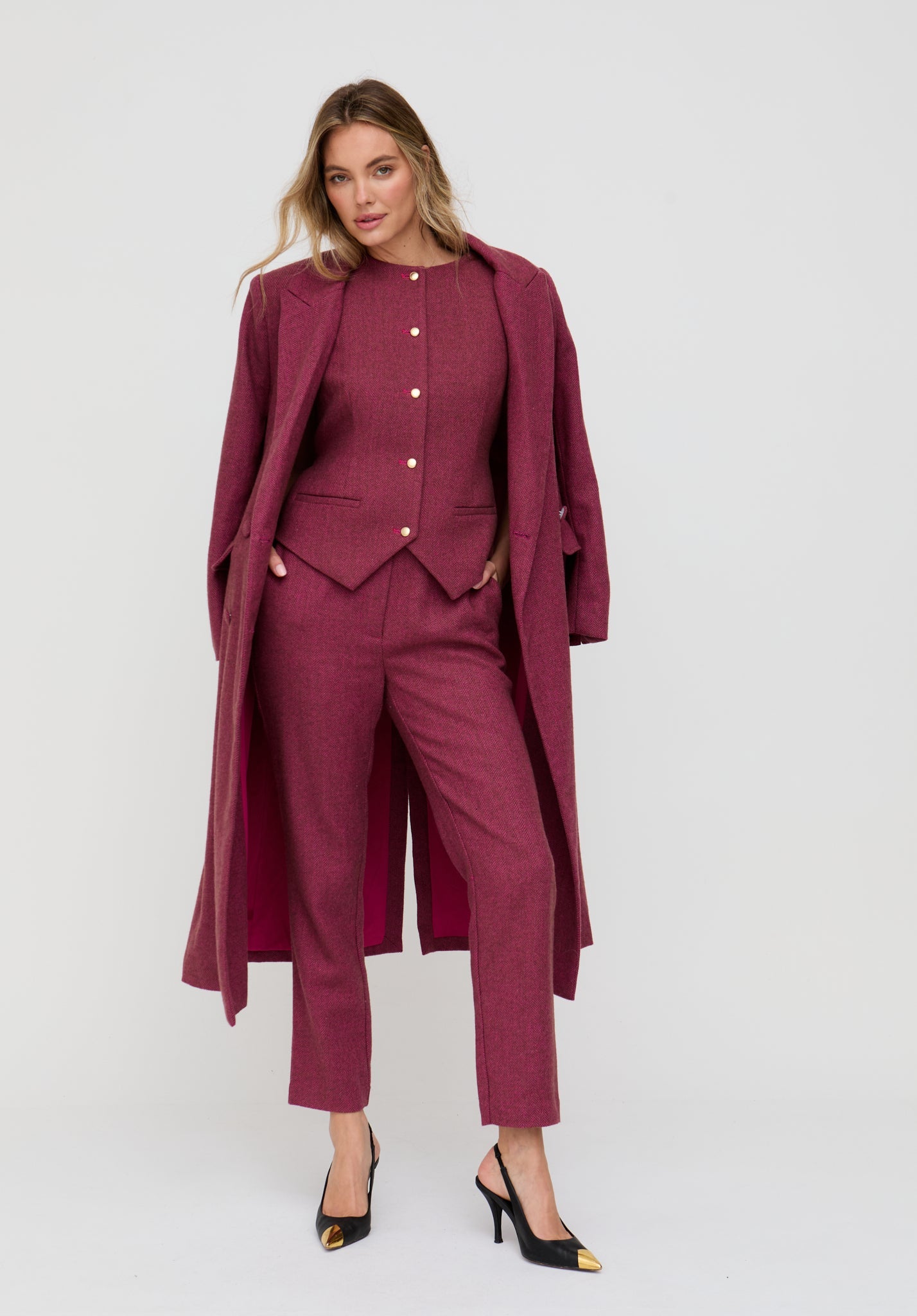 Woman wearing a burgundy suit with a long coat on a white background