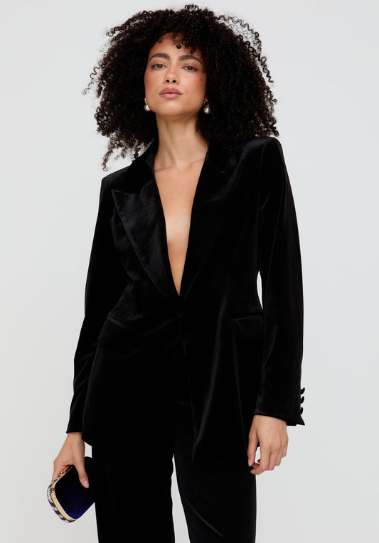 Woman wearing a black velvet suit with a plunging neckline on a light gray background