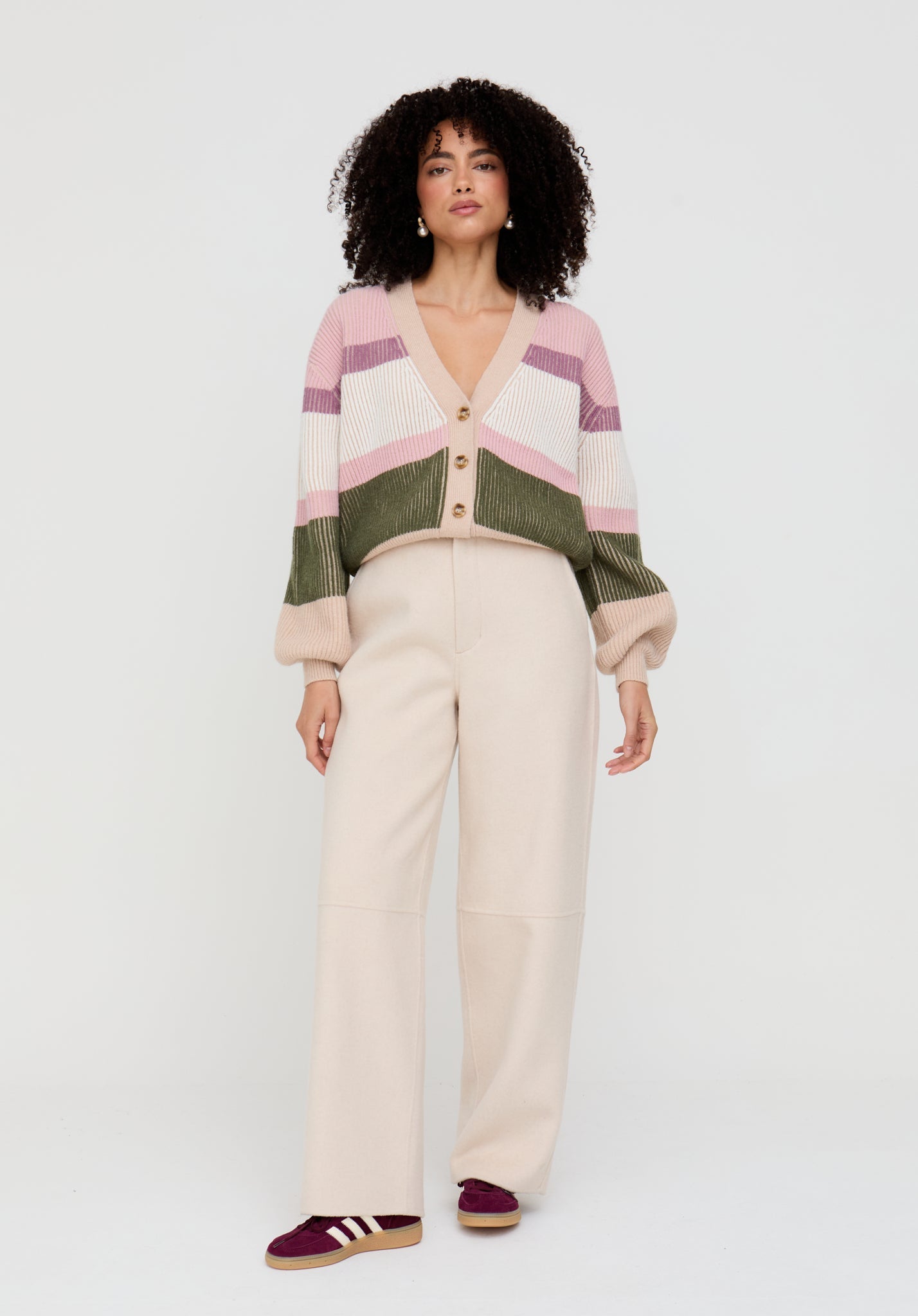 Woman wearing a striped cardigan and white pants on a white background