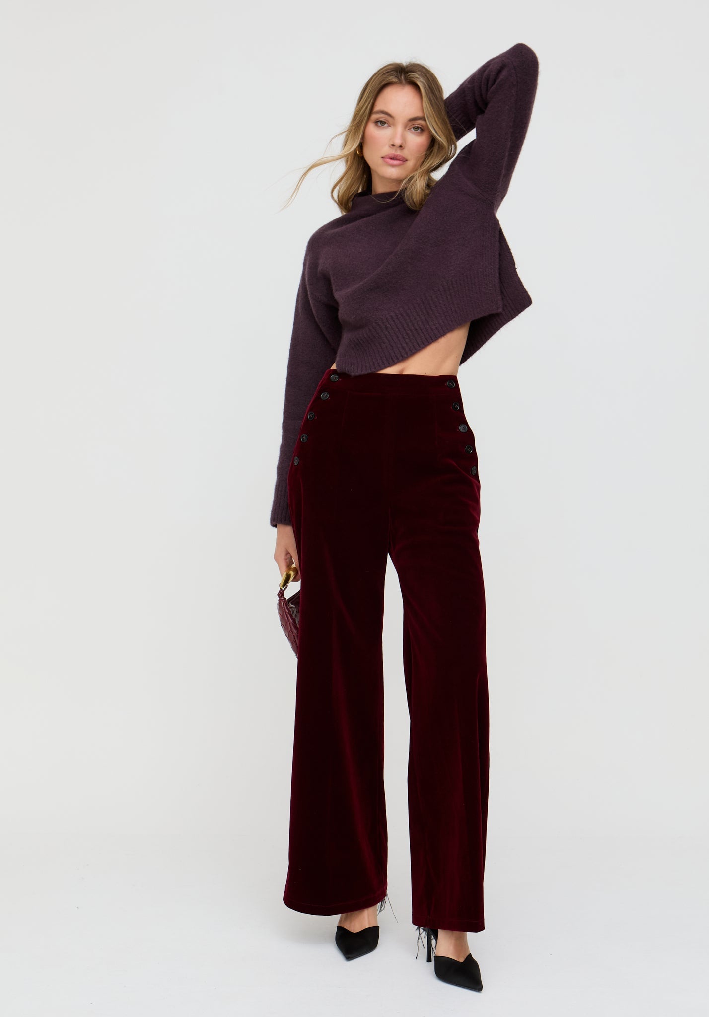 Woman wearing a dark purple turtleneck and wide-leg pants on a white background
