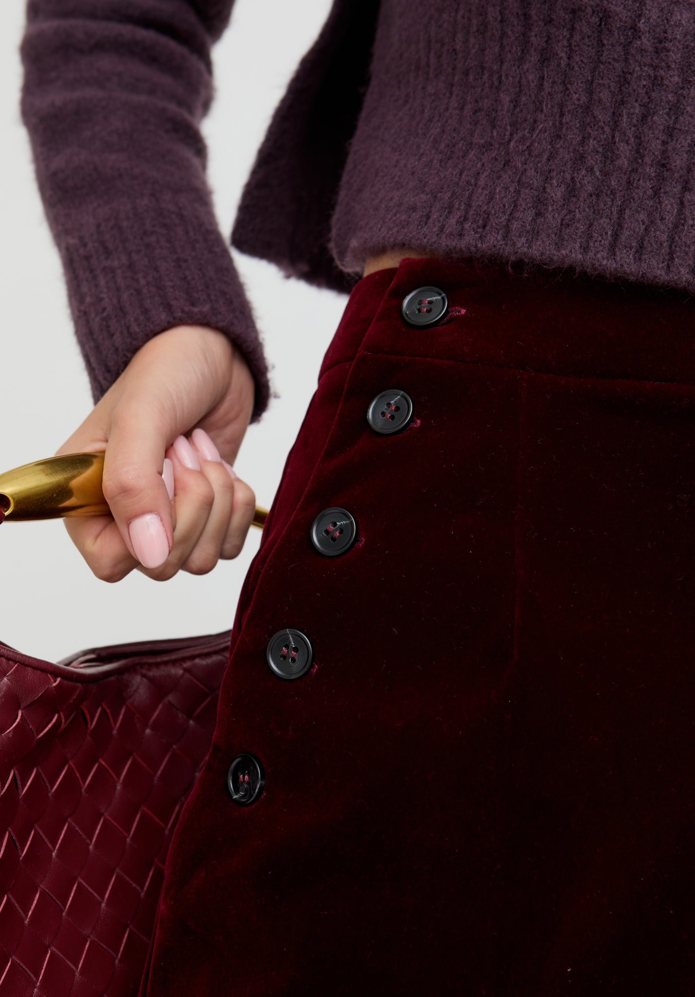 Close-up of a person holding a gold handle with a burgundy textured bag and sweater.