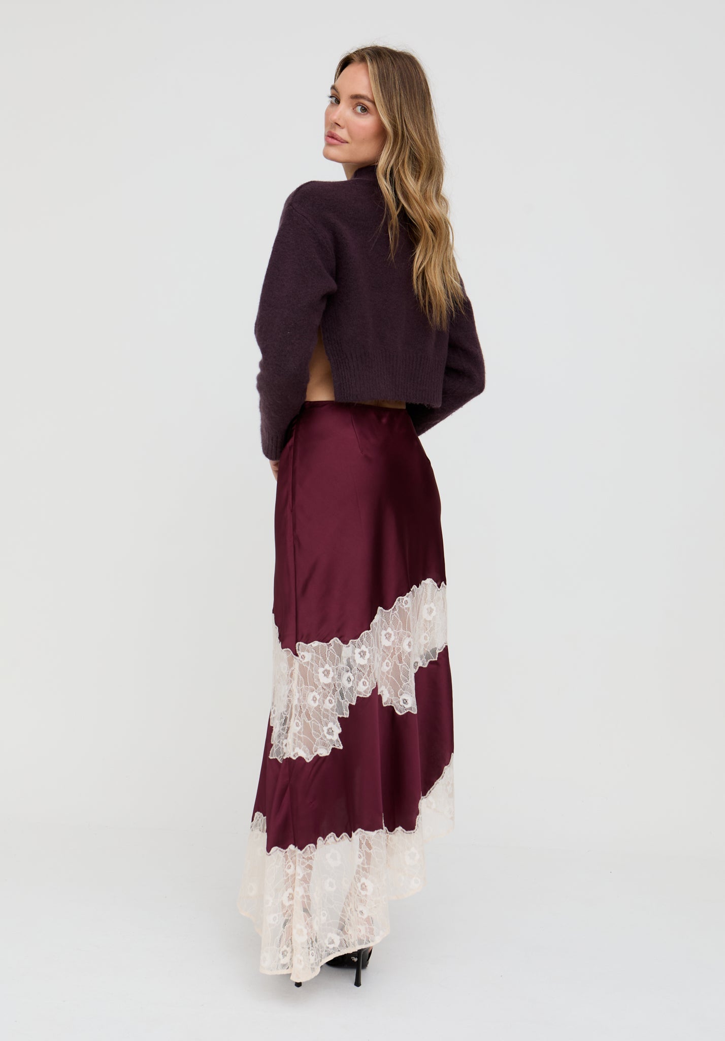 Woman wearing a burgundy sweater and skirt with lace details on a white background
