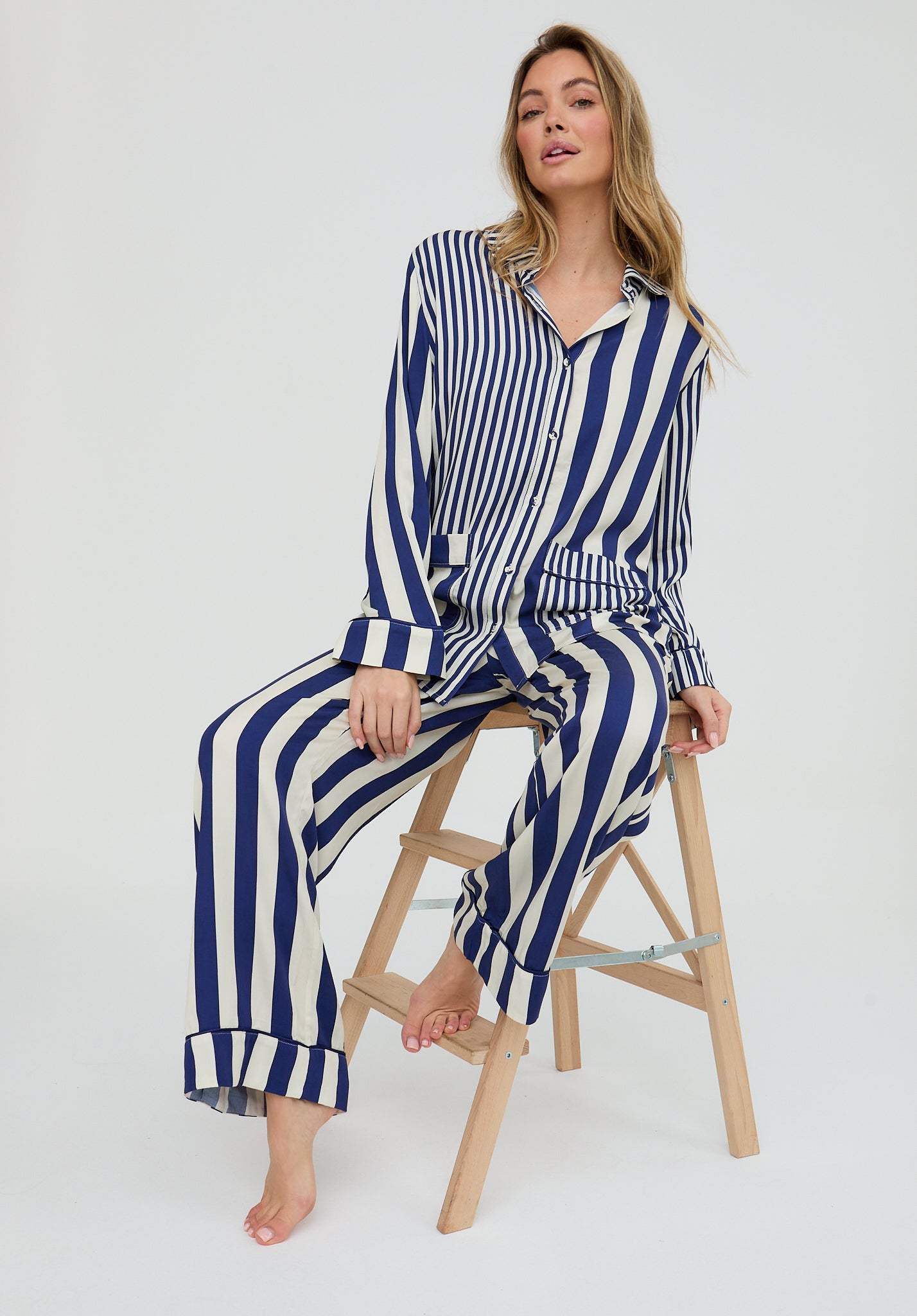 Woman wearing a blue and white striped outfit sitting on a wooden stool against a white background