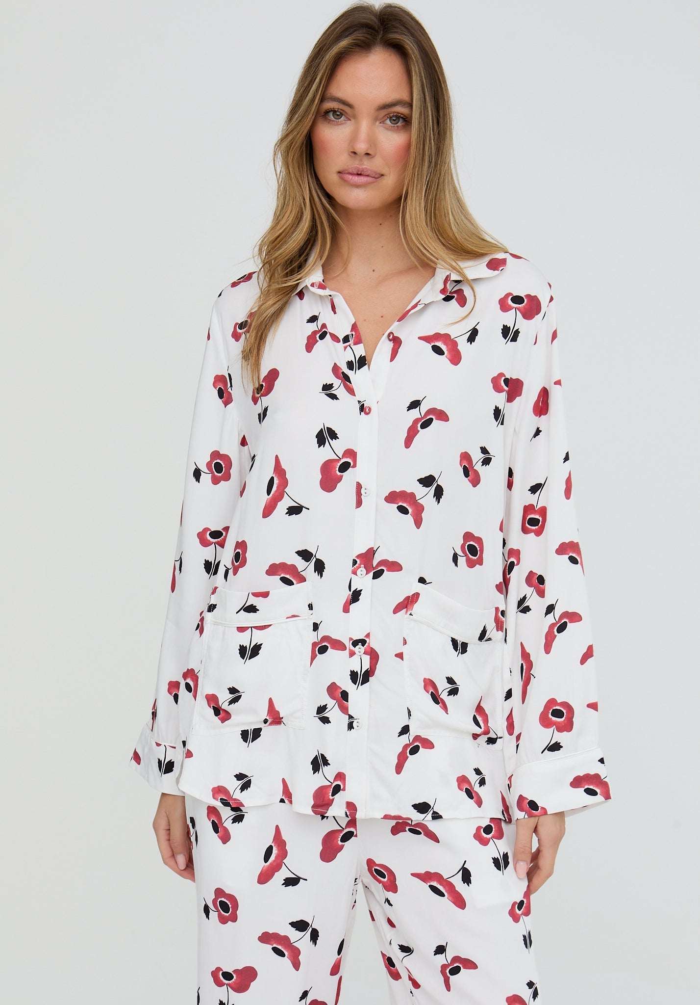 Woman wearing a white nightshirt with red floral pattern on a plain background