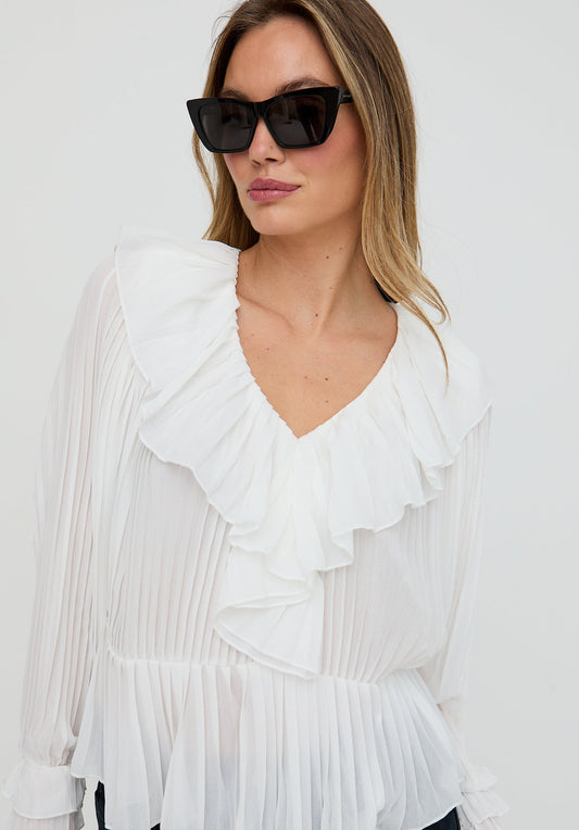 Woman wearing a white pleated blouse with ruffles and black sunglasses against a white background