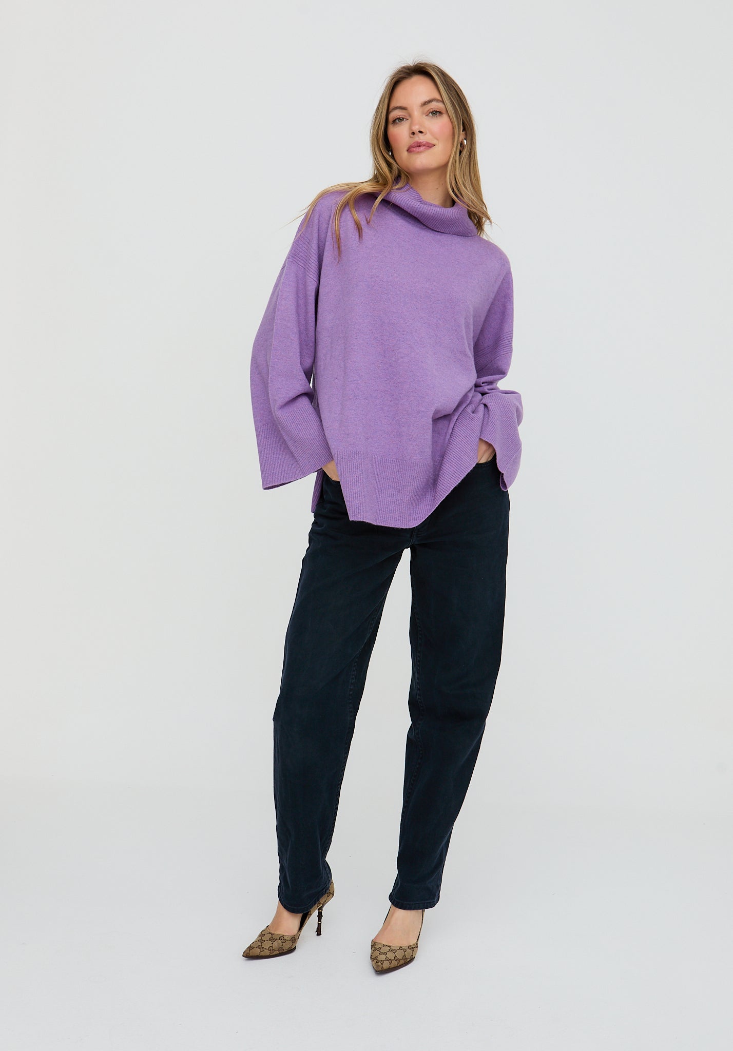 Woman wearing a purple sweater and black pants on a white background