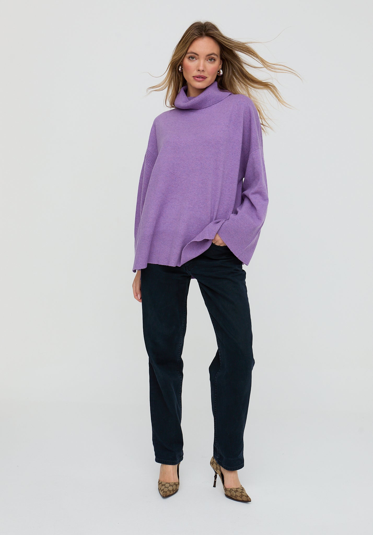 Woman wearing a purple sweater and dark jeans on a white background