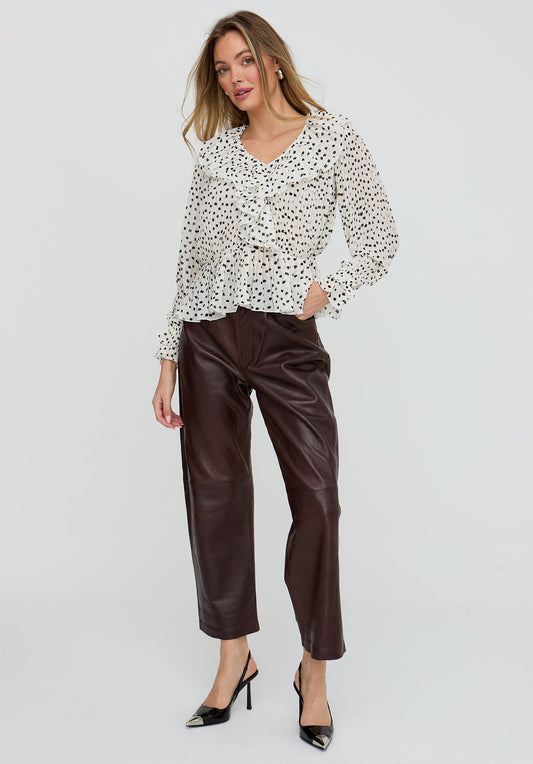 Woman wearing a patterned blouse and brown leather pants on a white background