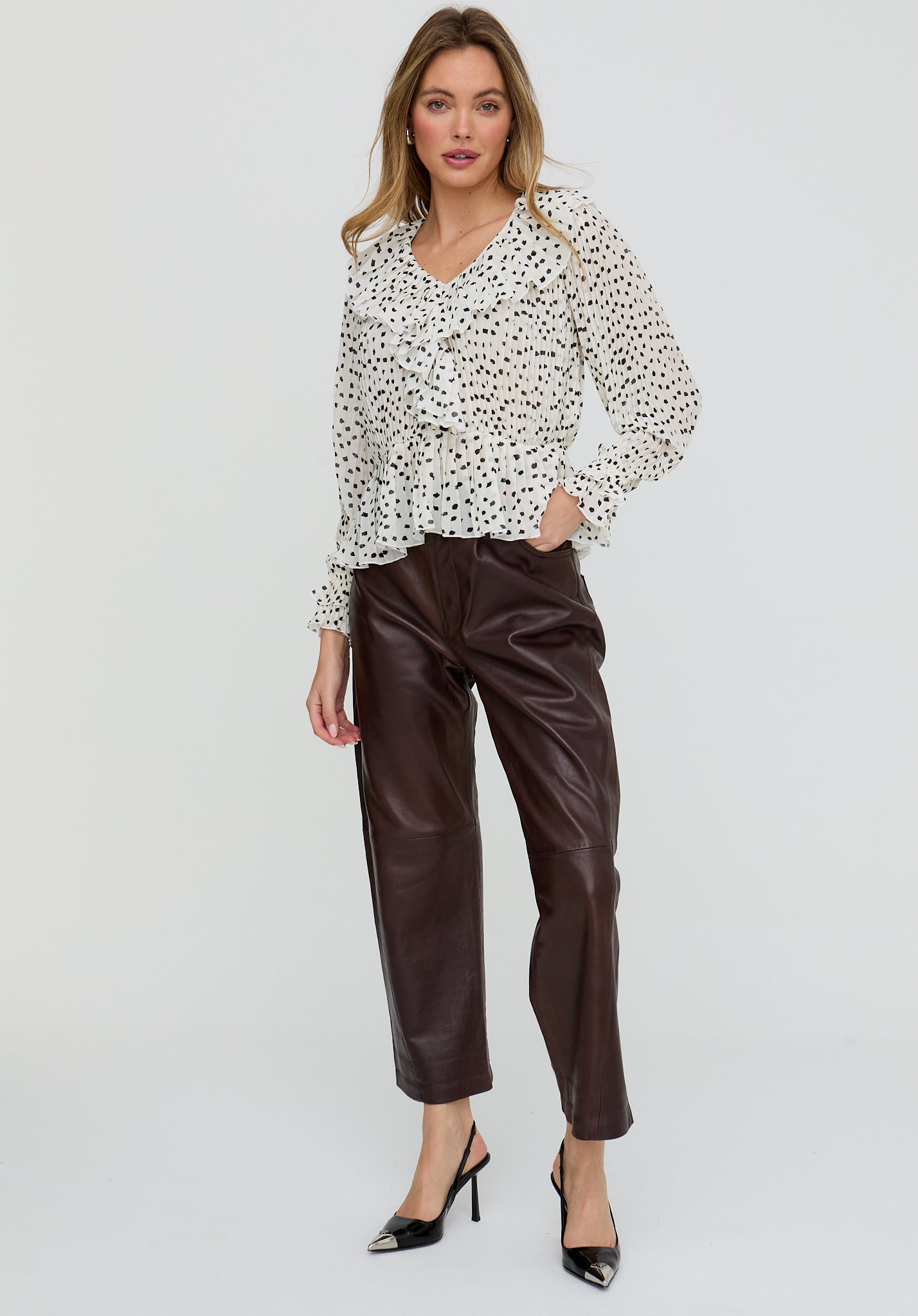 Woman wearing a patterned blouse and brown leather pants on a white background