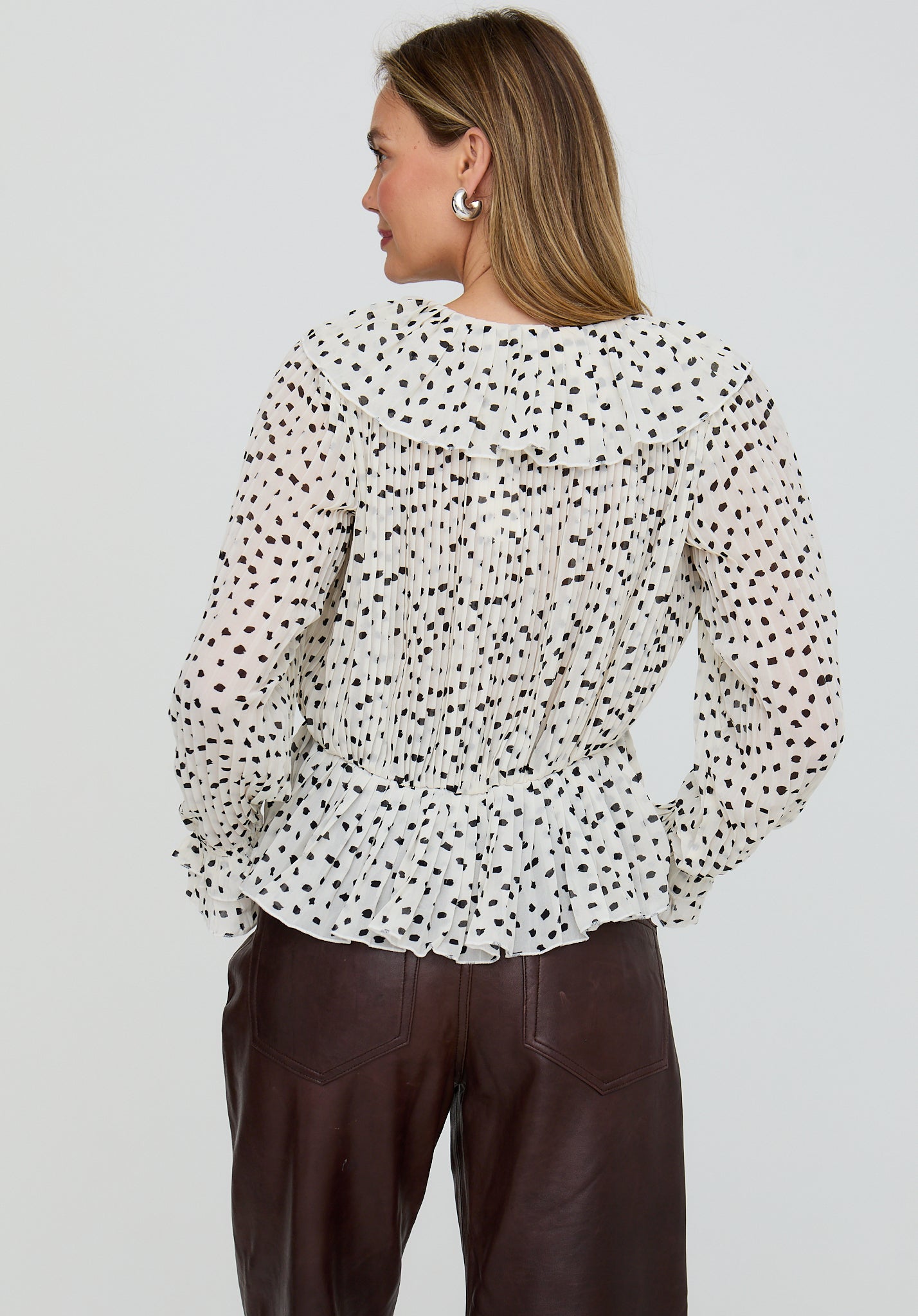 Woman wearing a polka dot blouse and brown pants on a plain background
