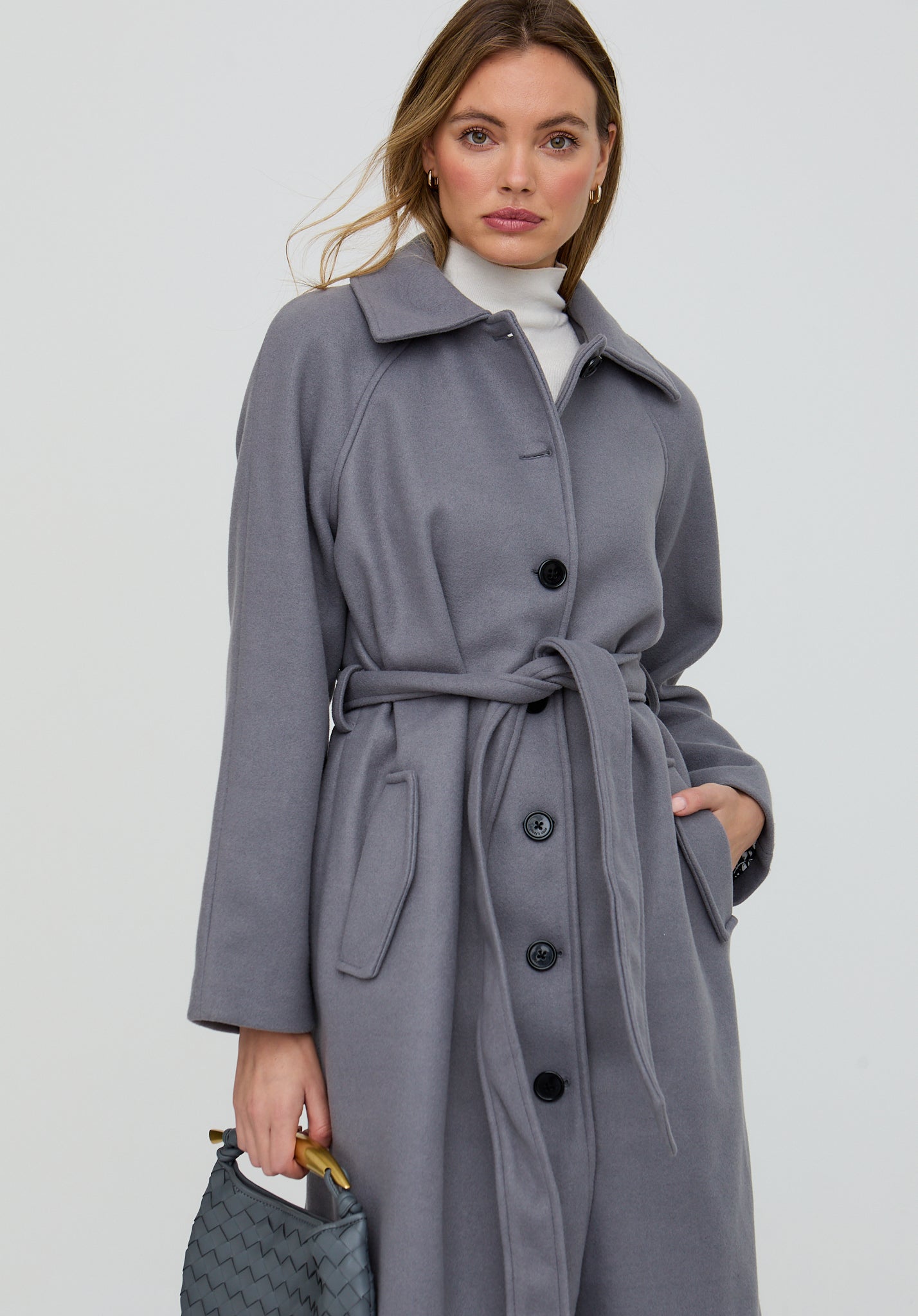 Woman wearing a gray coat with a belt on a plain background