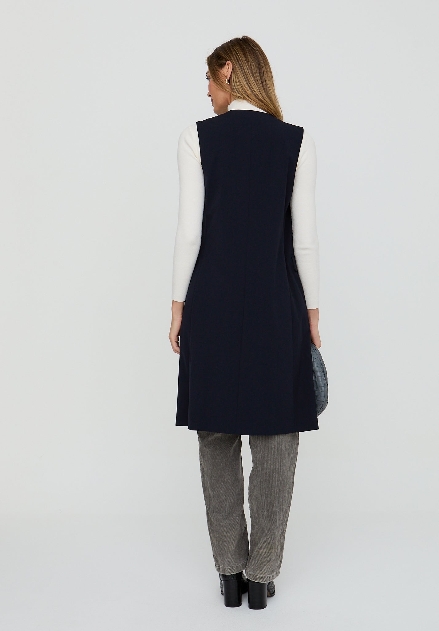 Woman wearing a navy vest over a white shirt and gray pants on a white background