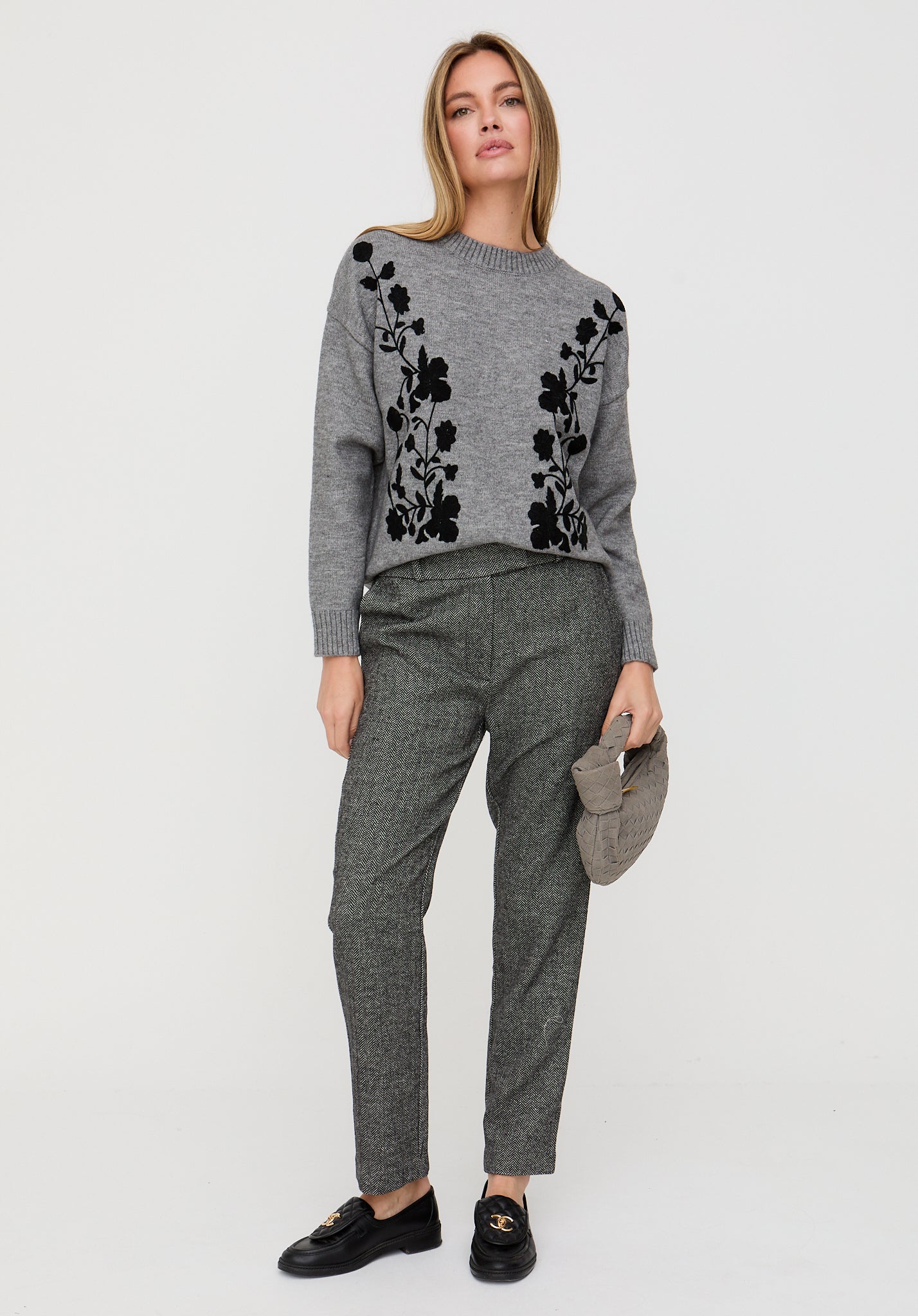 Woman wearing a gray sweater with black floral patterns and gray pants on a white background