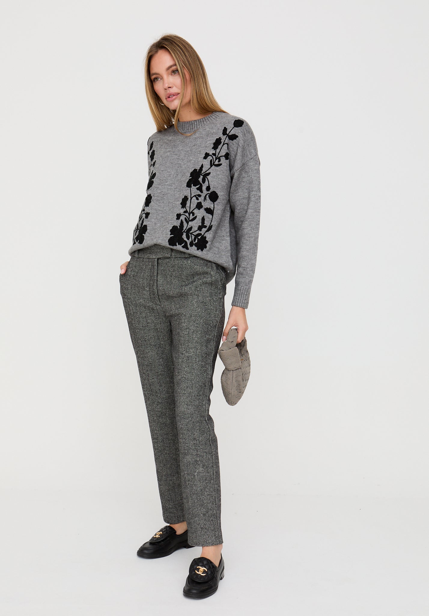 Woman wearing a gray sweater with black floral patterns and gray pants on a white background