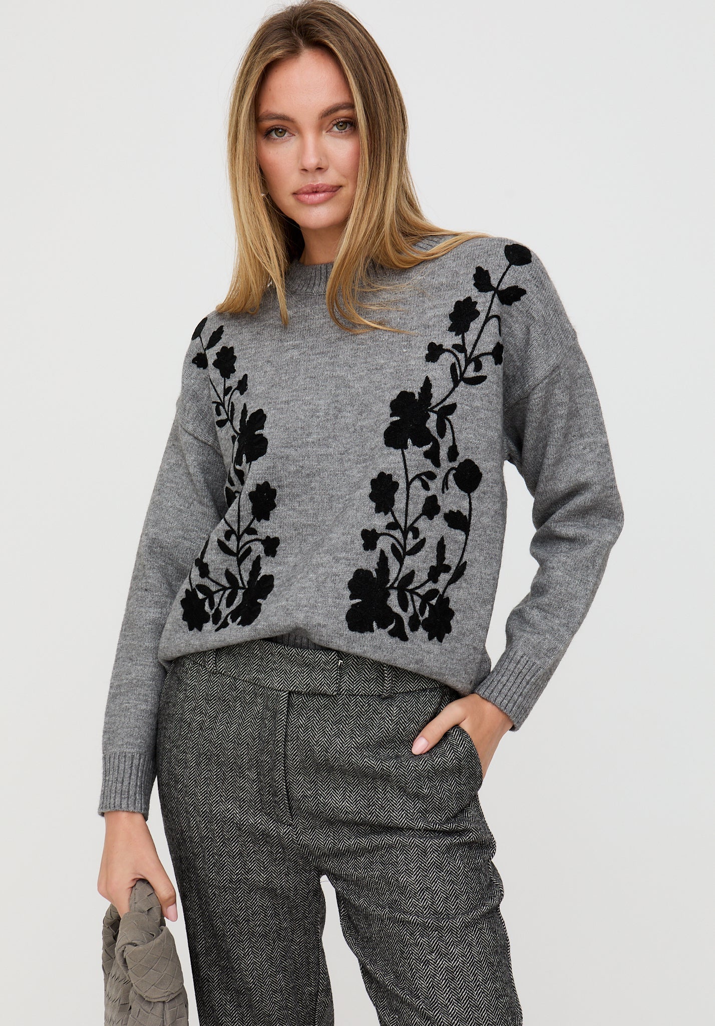 Woman wearing a gray sweater with black floral patterns on a light gray background