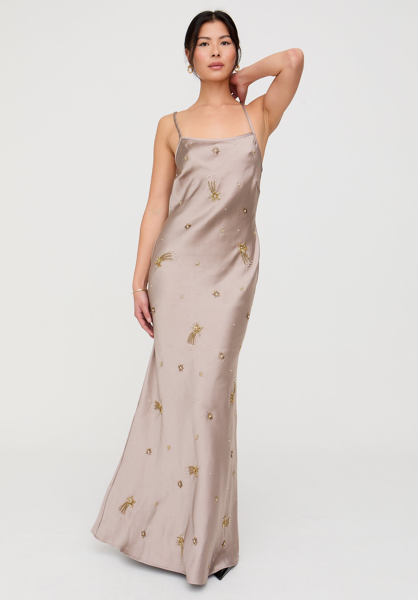 Woman wearing a beige slip dress with gold embroidery on a white background