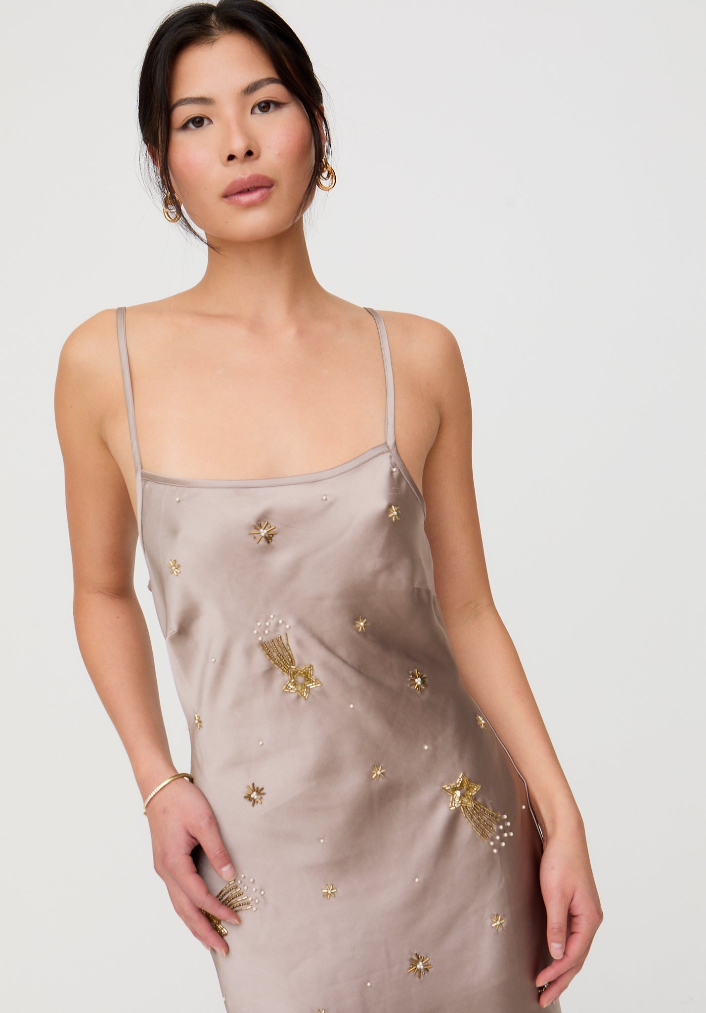 Woman wearing a beige satin slip dress with gold floral embroidery on a plain background