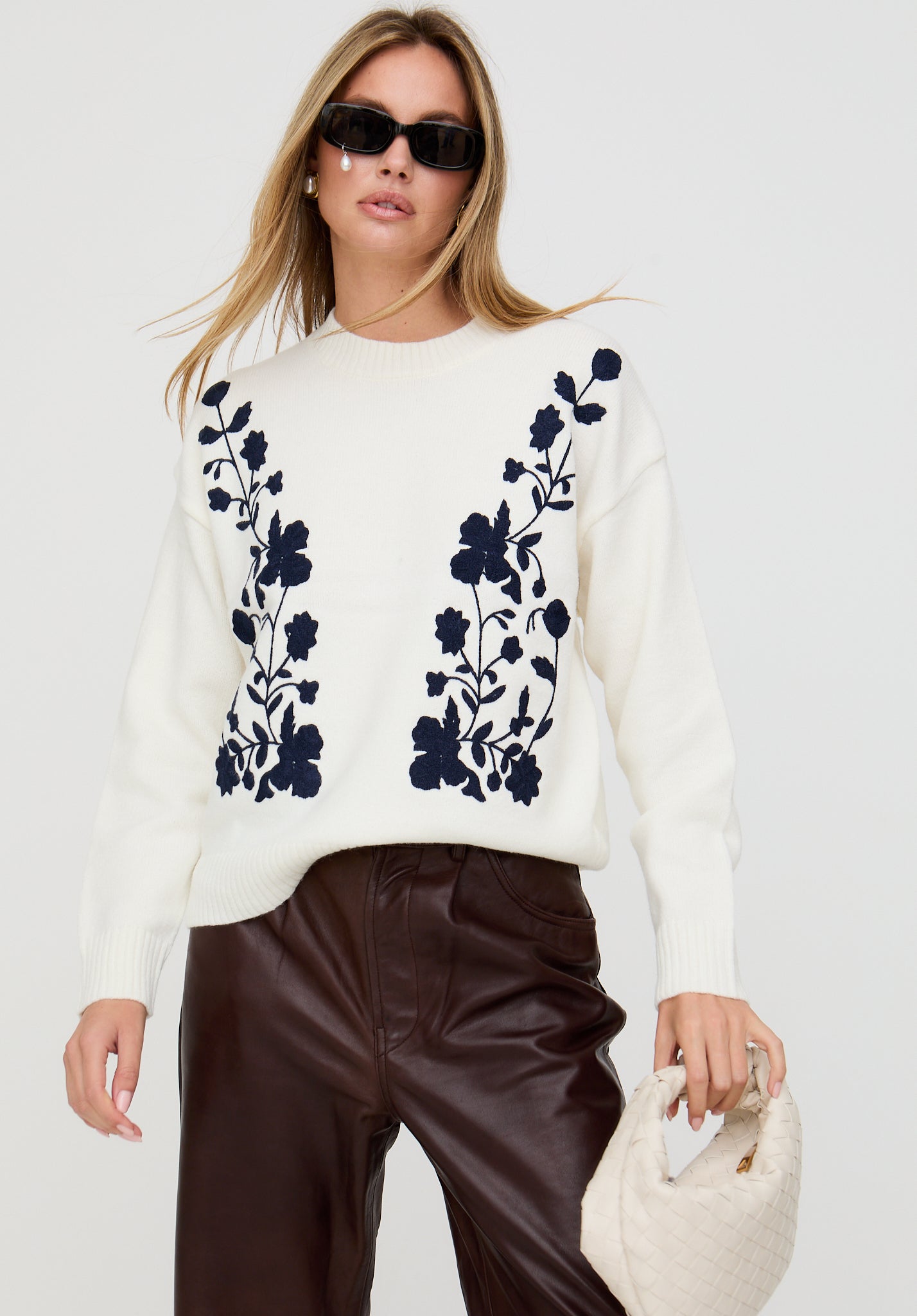 Woman wearing a white sweater with black floral patterns on a plain background