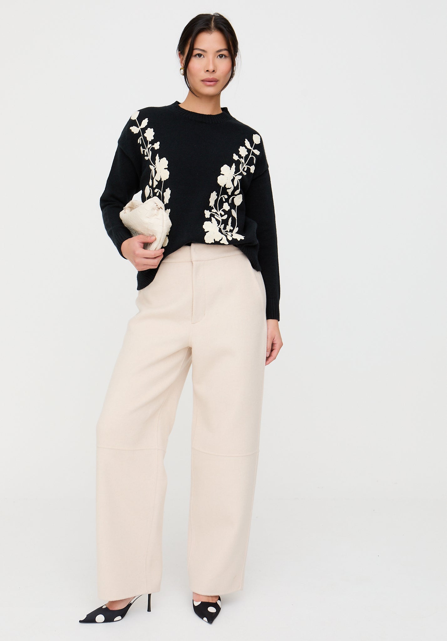 Woman wearing a black sweater with white floral patterns and beige pants on a white background