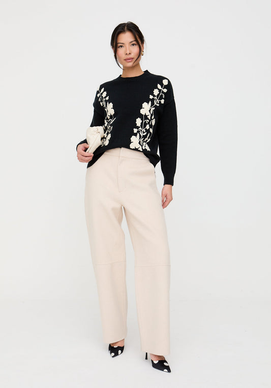 Woman wearing a black sweater with floral embroidery and beige pants on a white background