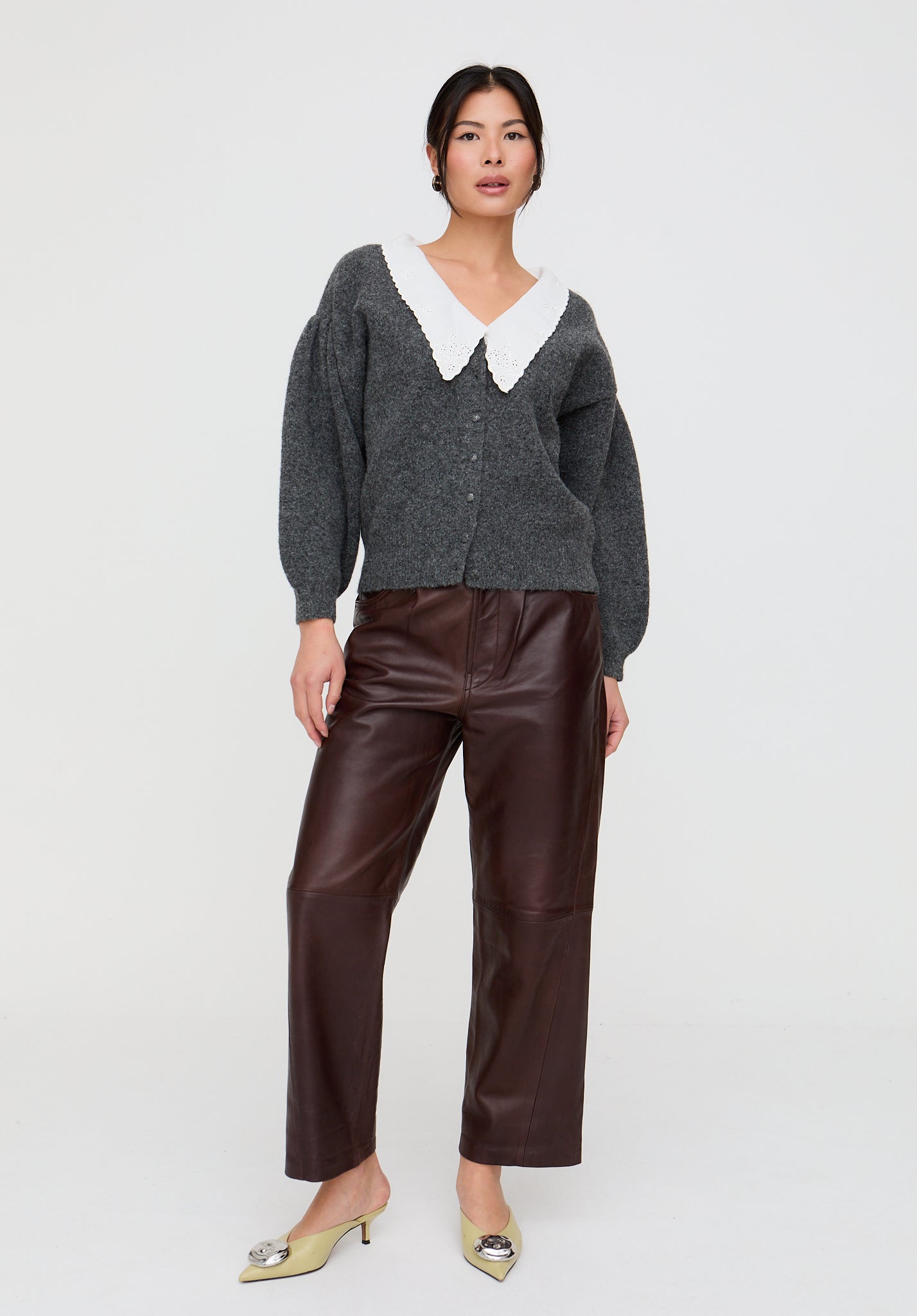 Woman wearing a gray cardigan with a white collar and brown leather pants on a white background