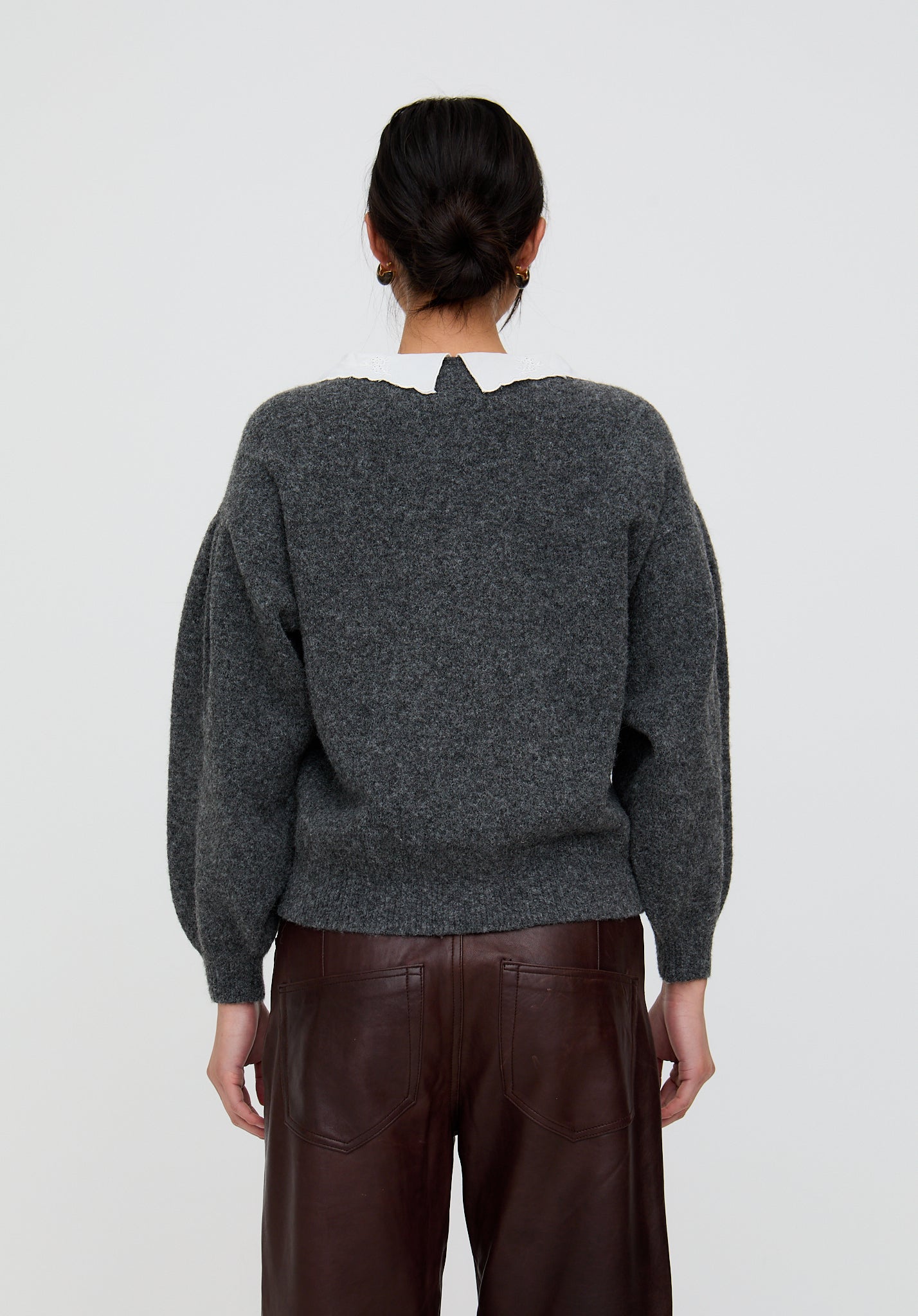 Person wearing a dark gray sweater and brown pants on a light gray background