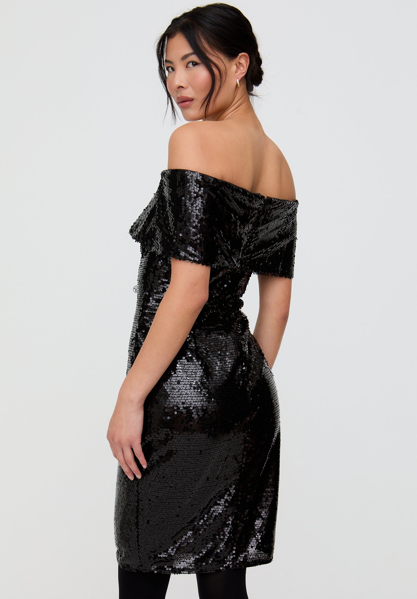 Woman wearing a black sequin off-shoulder dress on a white background