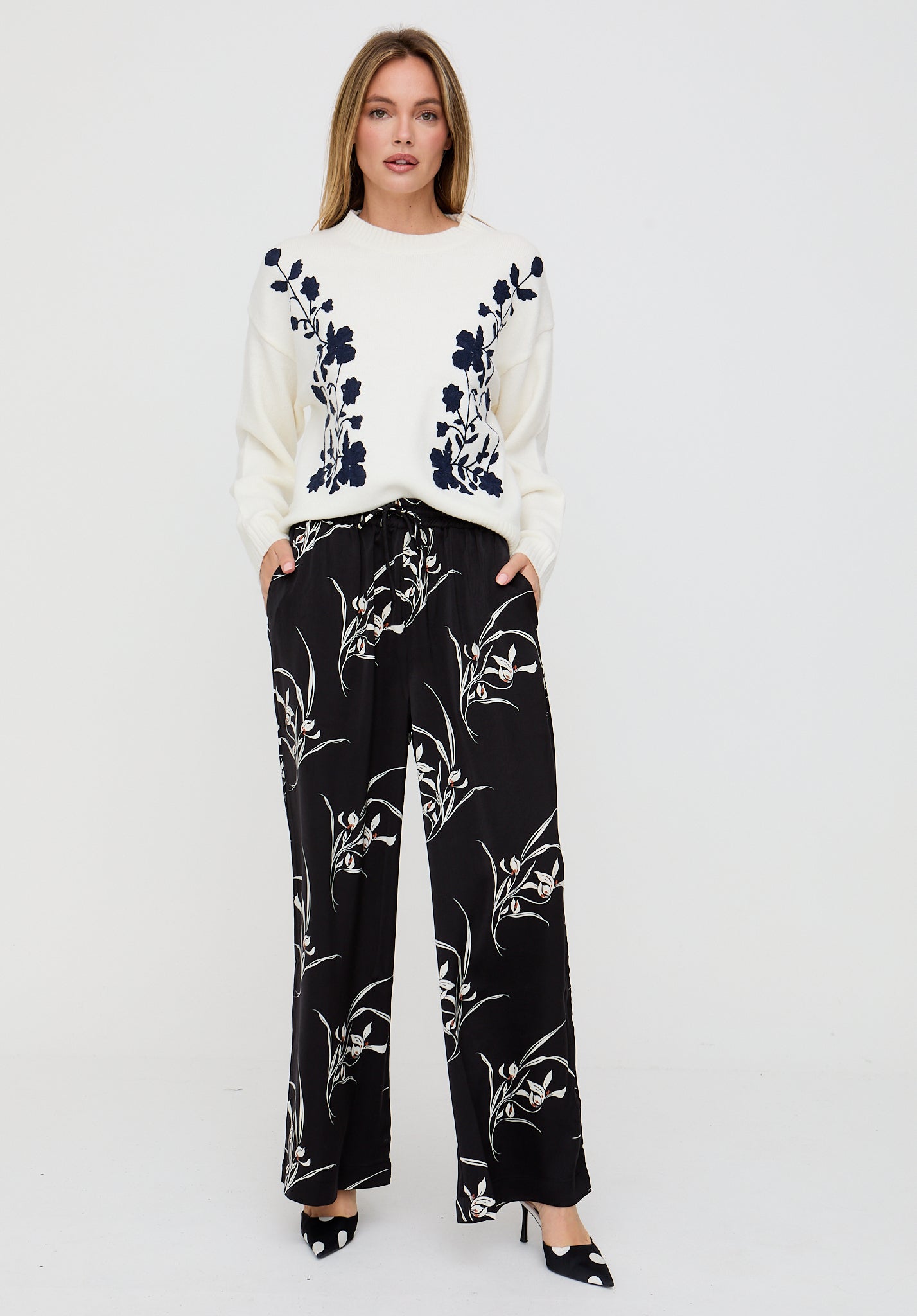 Woman wearing a white sweater with black floral patterns and black pants with white floral patterns on a white background